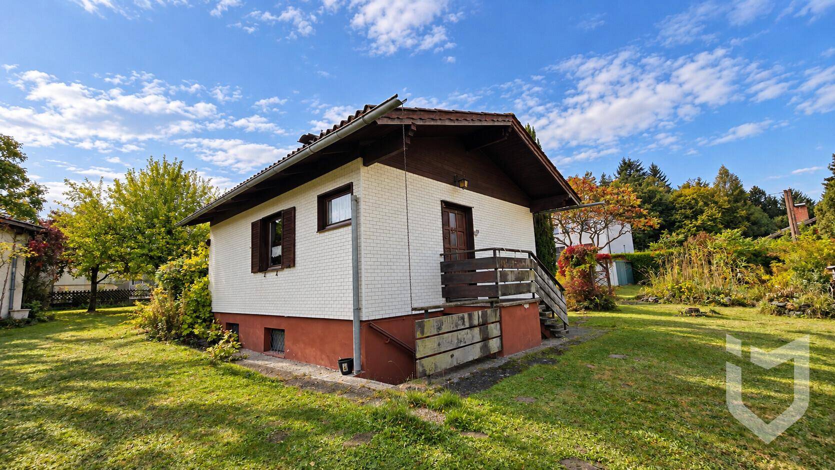 Ansicht des Einfamilienhauses mit weißer Fassade, braunem Dach und kleinem Balkon.
