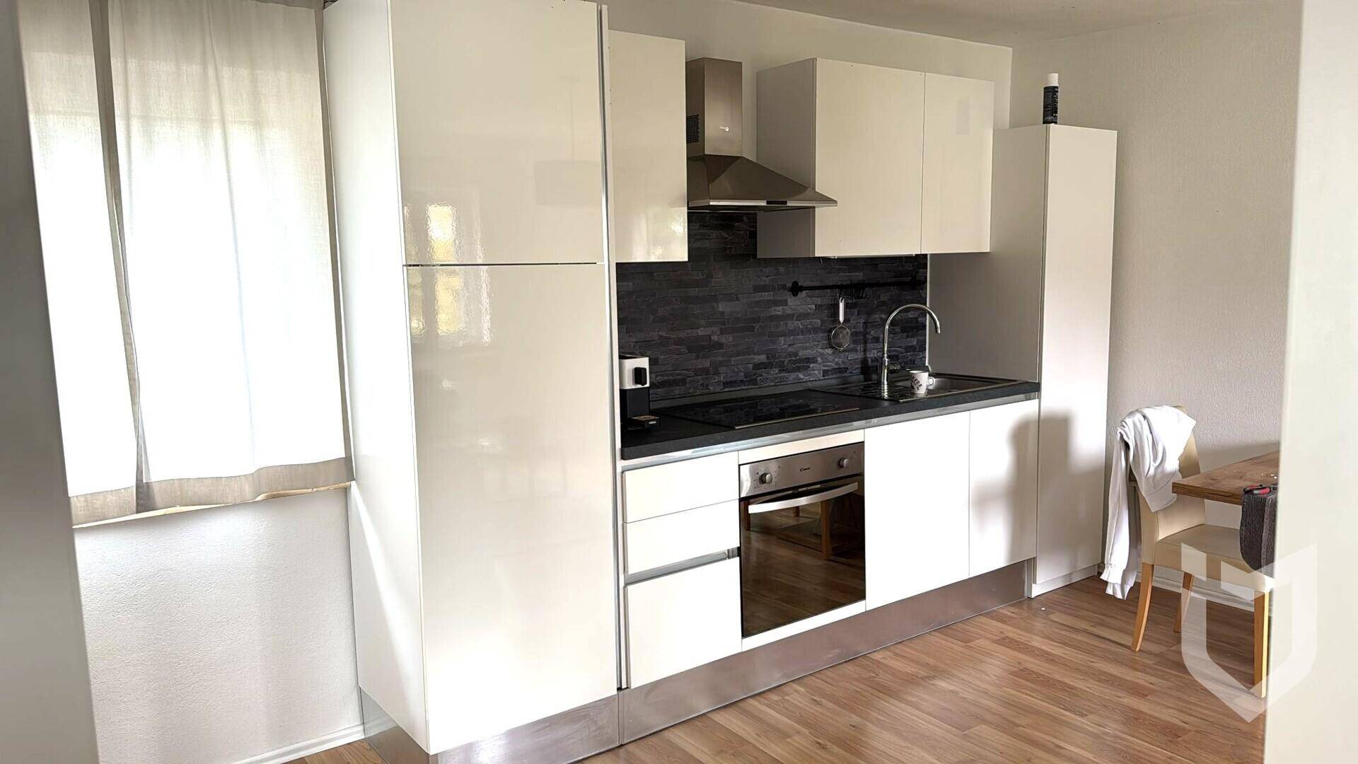 Moderne weiße Küche mit Hochglanzfronten, dunkler Rückwand und integriertem Backofen.
