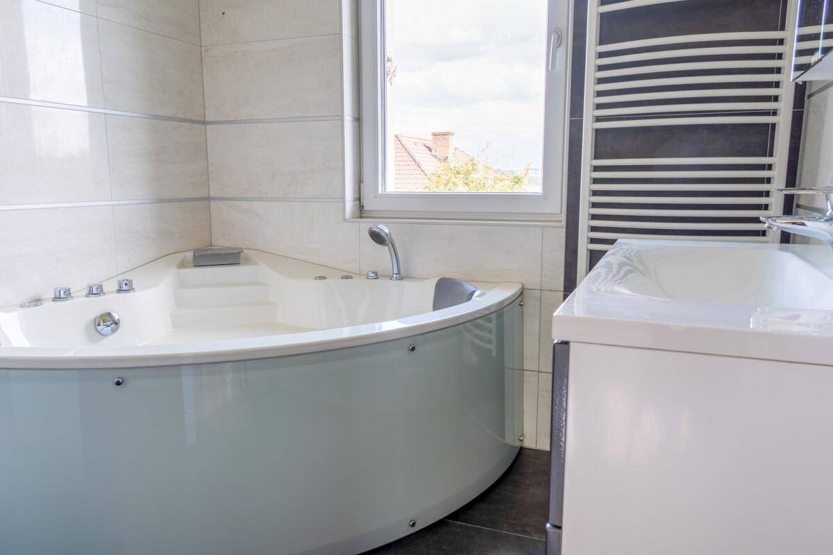 Badezimmer mit Eckbadewanne, Waschbecken und beheiztem Handtuchhalter, hell gefliest.