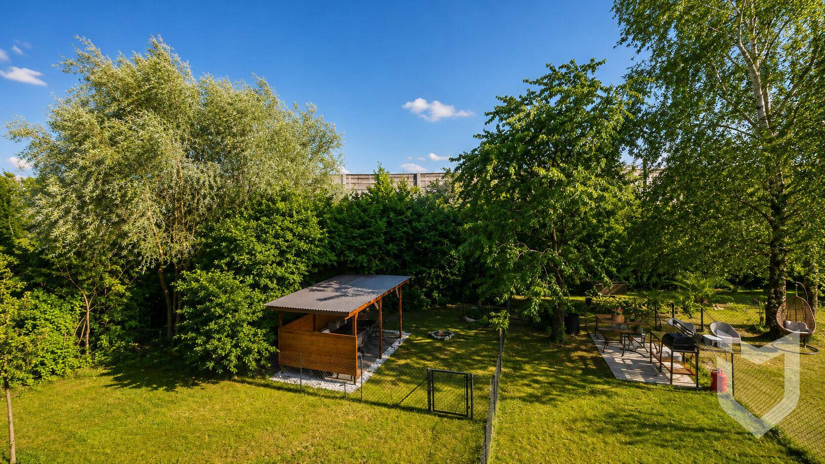 Großer, gepflegter Garten mit Rasenfläche, Baumbestand, einer Holzpergola und einem Grillbereich.