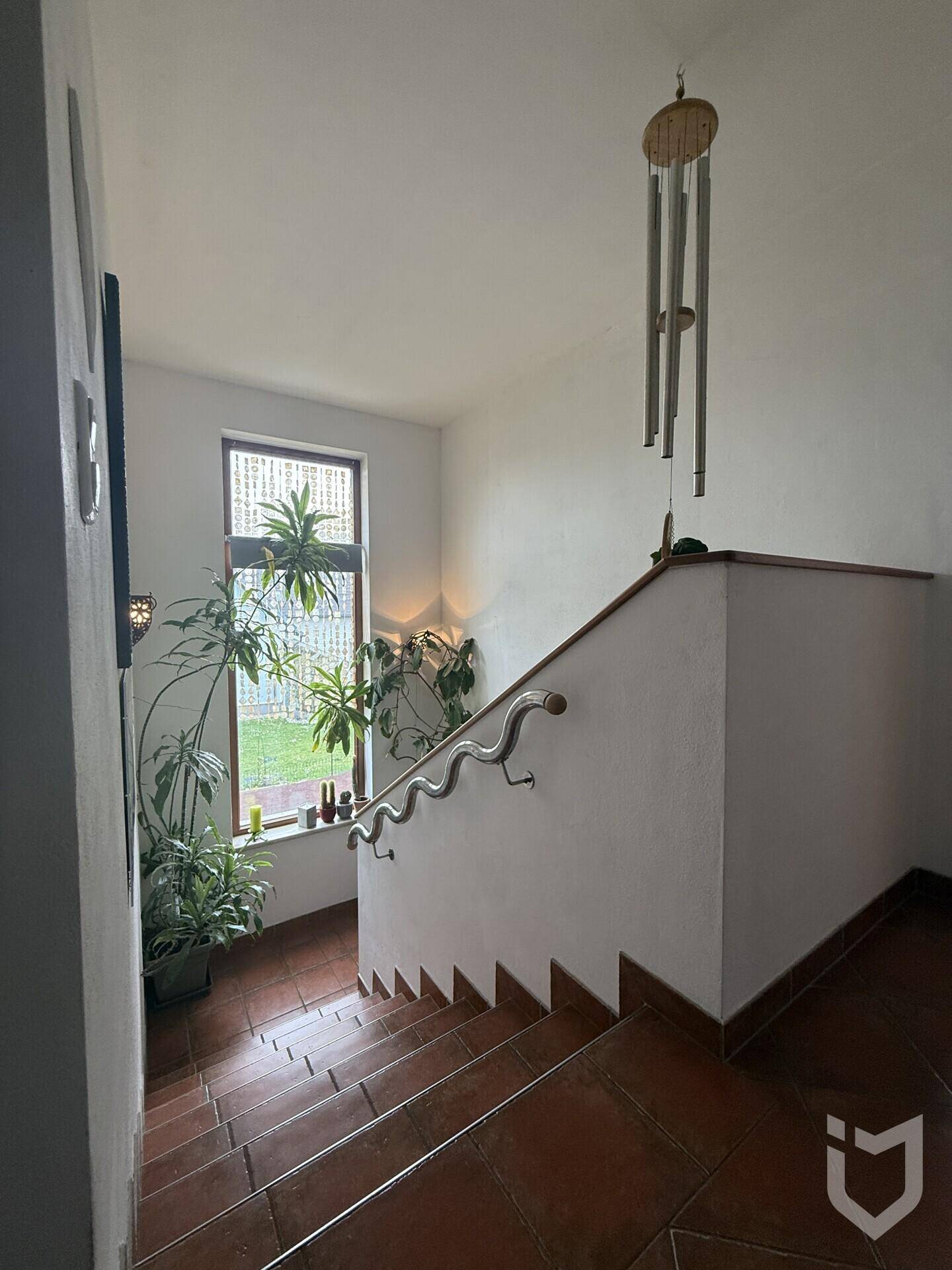 Helles Treppenhaus mit Terrakotta-Fliesenstufen und einem Fenster, das viel Grün hereinlässt.