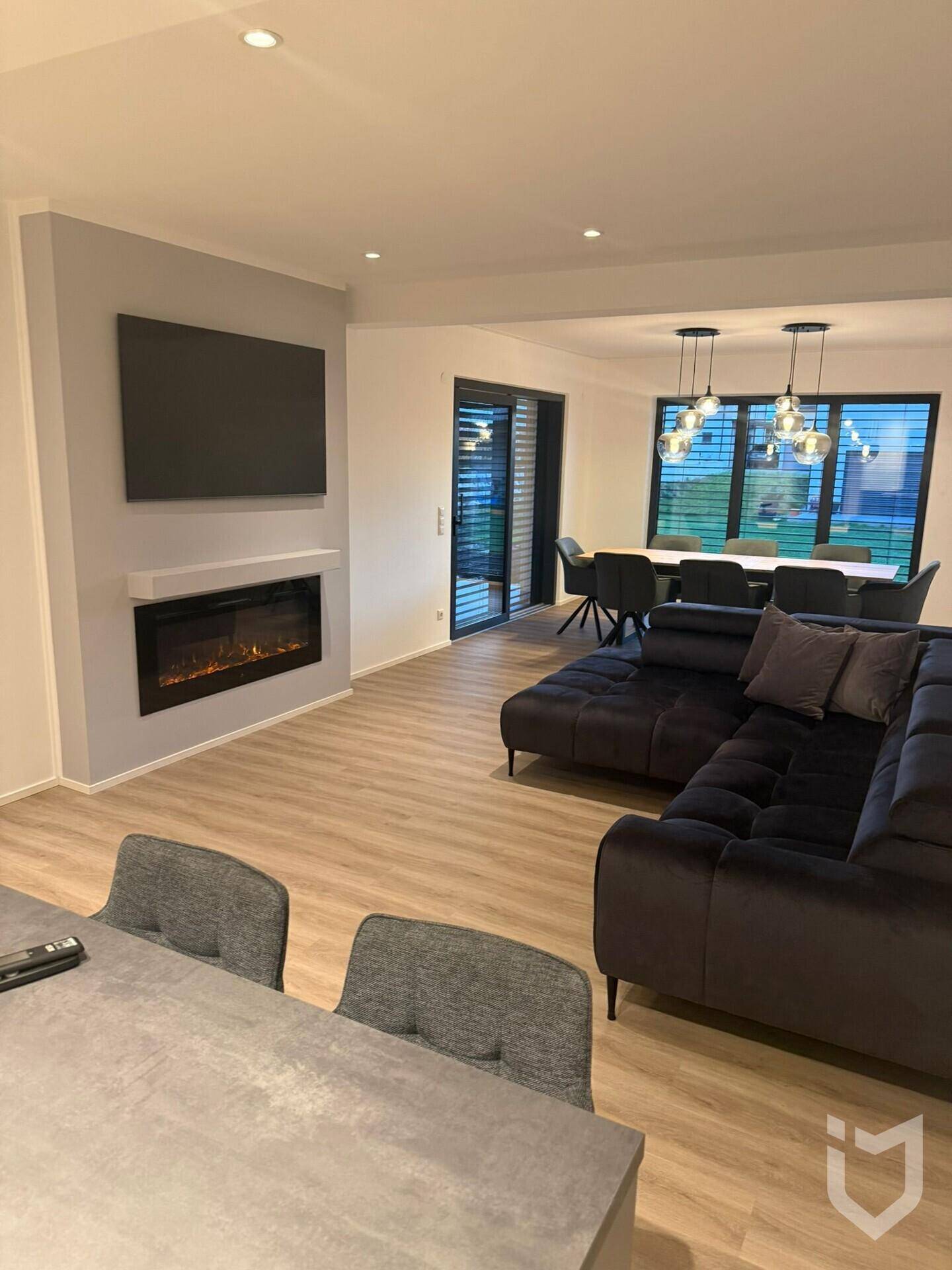 Gemütlicher Wohn- und Essbereich mit dunklem Sofa, Kamin und Blick nach draußen.