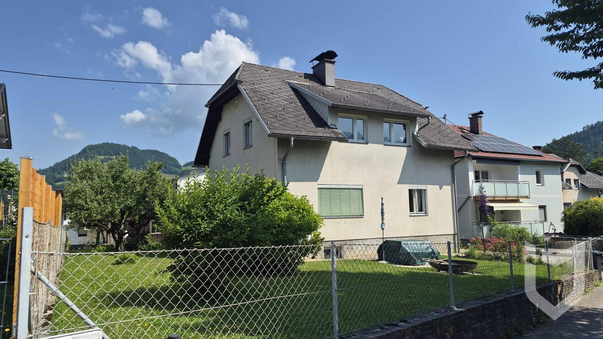 Vorderansicht des Hauses mit umzäuntem Garten und Blick auf die umliegende Landschaft.