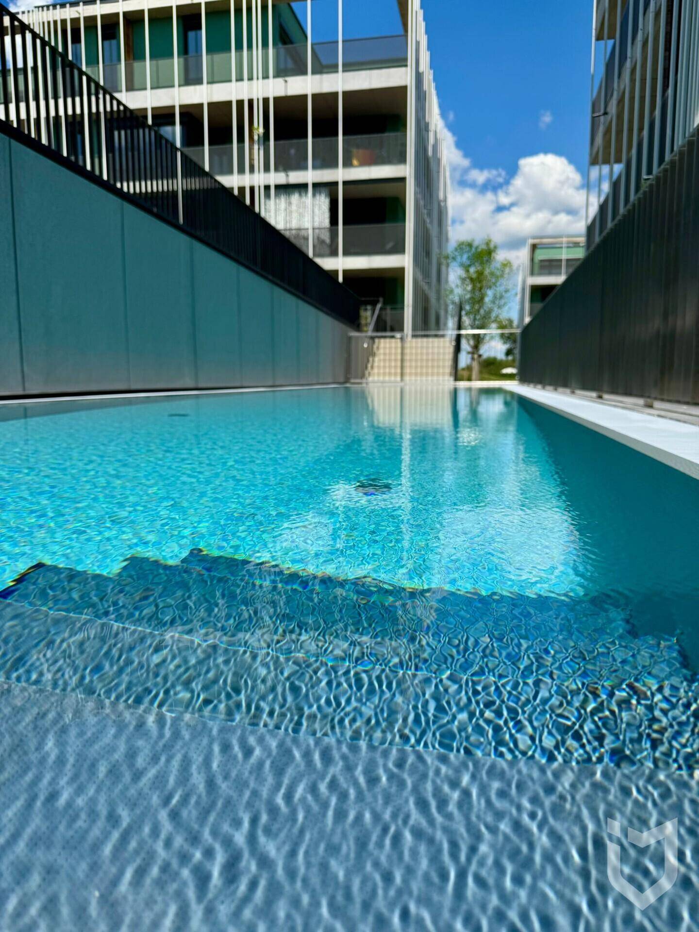 Außenpool mit klarem Wasser und Stufen, umgeben von moderner Architektur und Grünflächen.