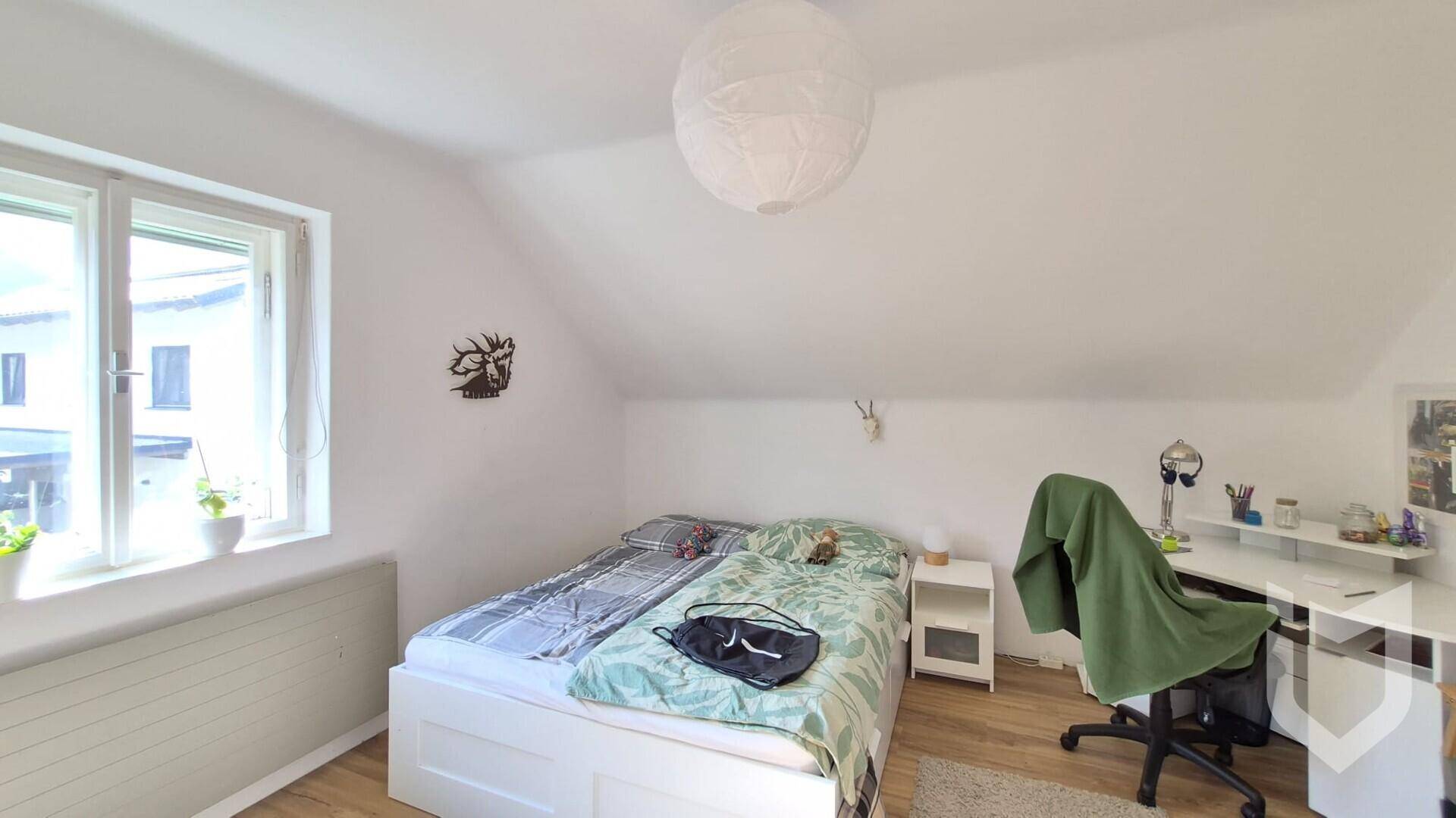 Schlafzimmer im Dachgeschoss mit schräger Decke, Bett und Schreibtisch am Fenster.