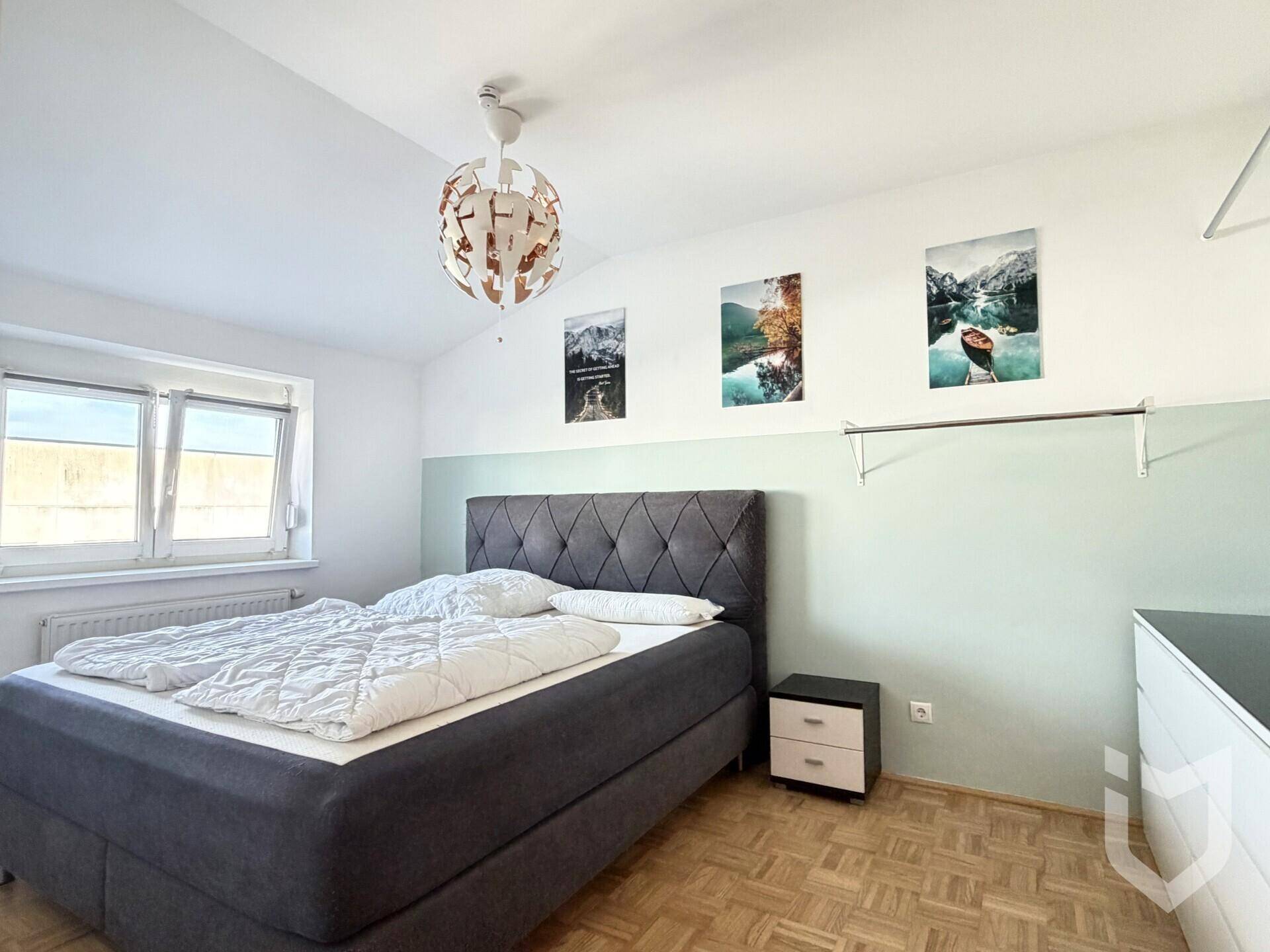 Schlafzimmer mit Doppelbett, Nachttisch, Parkettboden und einem Fenster für natürliche Belichtung.