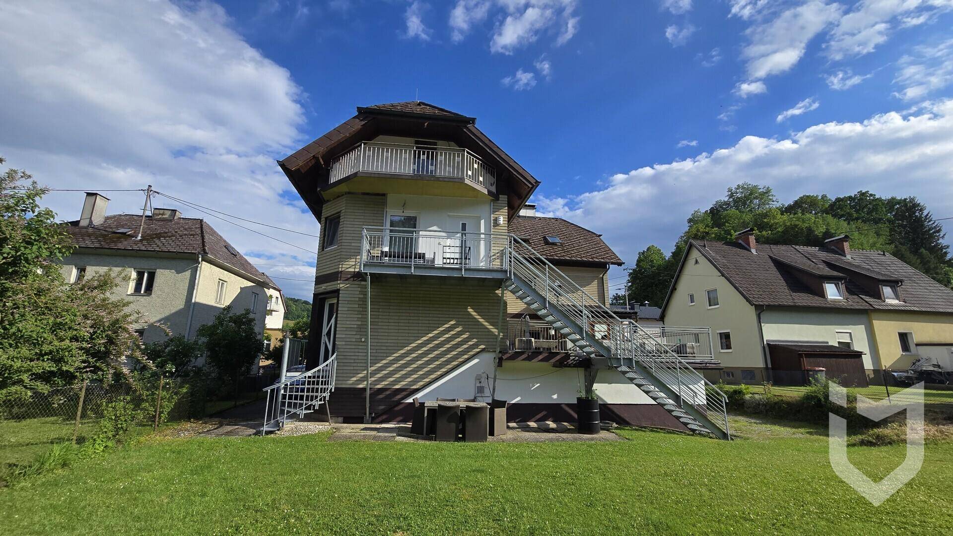 Seitenansicht des Gebäudes mit großem Gartenbereich und Außentreppen.