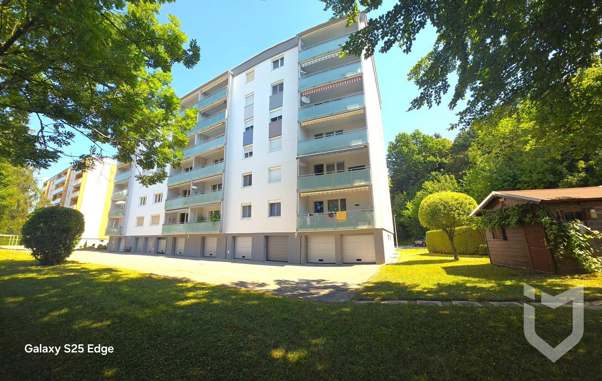 Mehrfamilienhaus mit mehreren Balkonen, umgeben von Bäumen und einer gepflegten Rasenfläche.