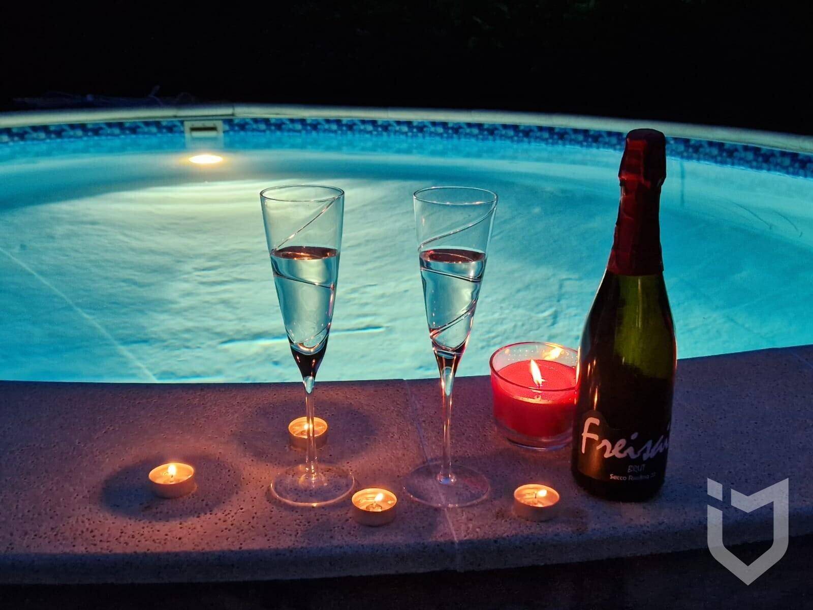 Sektgläser und Kerzen am Rand des beleuchteten Pools für eine romantische Atmosphäre.