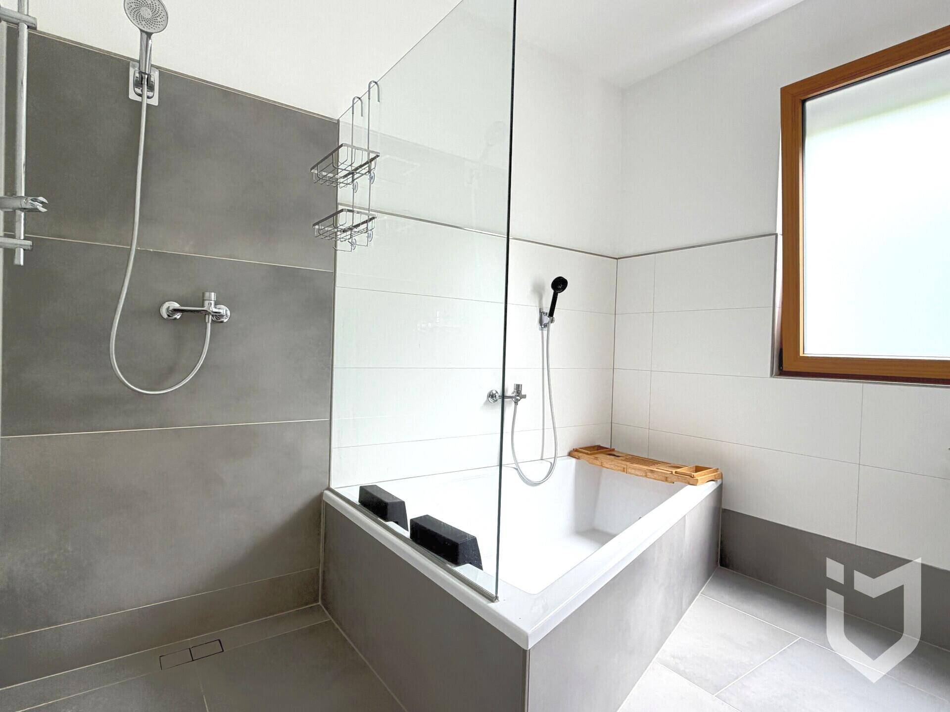 Modernes Badezimmer mit begehbarer Dusche, Eckbadewanne, grauen Fliesen und einem Fenster für Tageslicht.