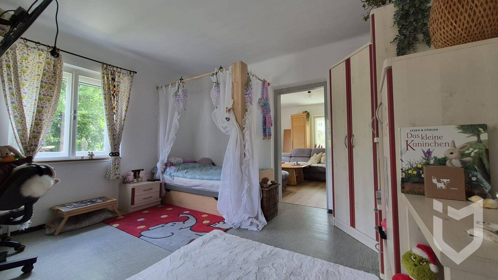 Kinderzimmer mit Himmelbett, Kleiderschrank und Zugang zu einem weiteren Wohnbereich.