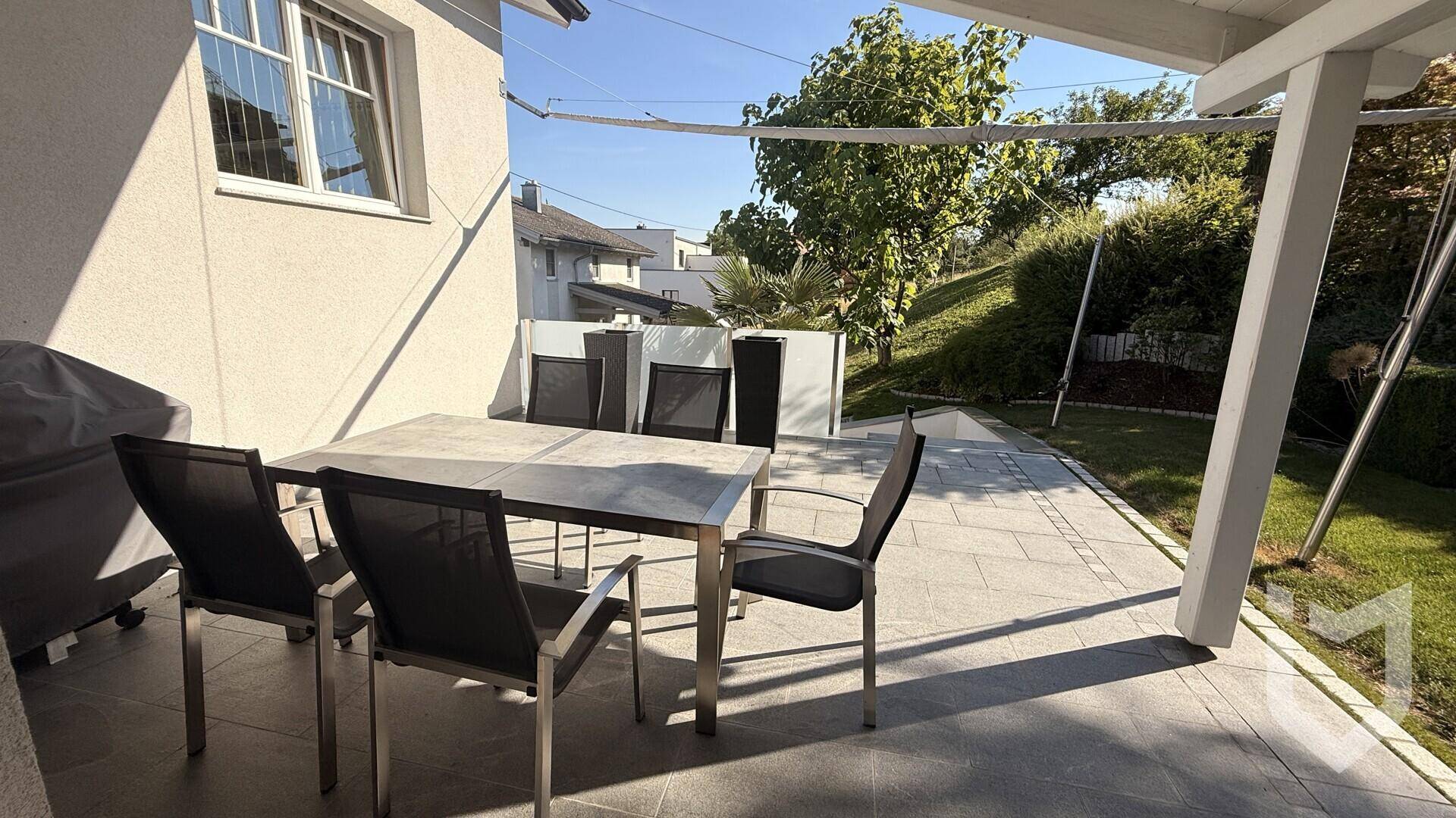 Überdachte Terrasse mit Esstisch und Stühlen, ideal für Mahlzeiten im Freien.