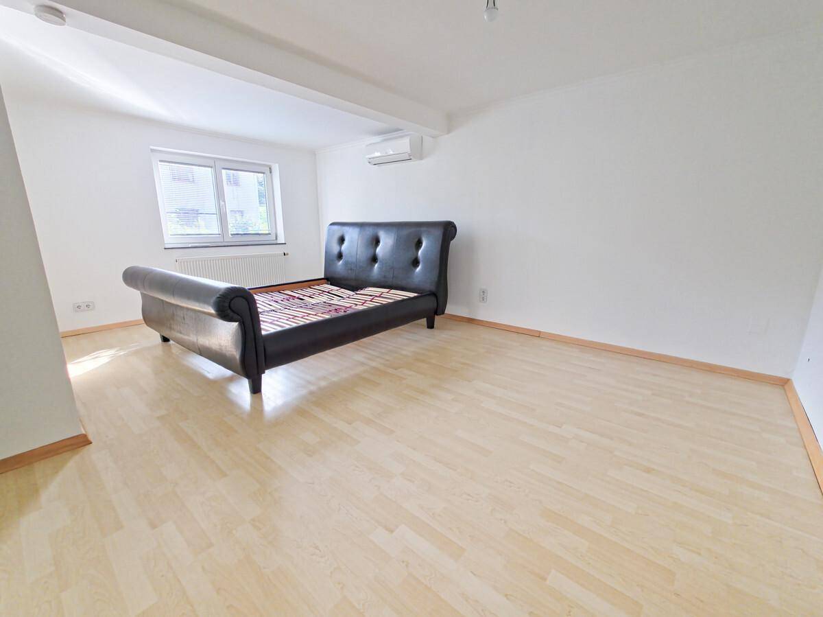 Geräumiges Schlafzimmer mit hellem Parkettboden, einem Bett und Klimaanlage.