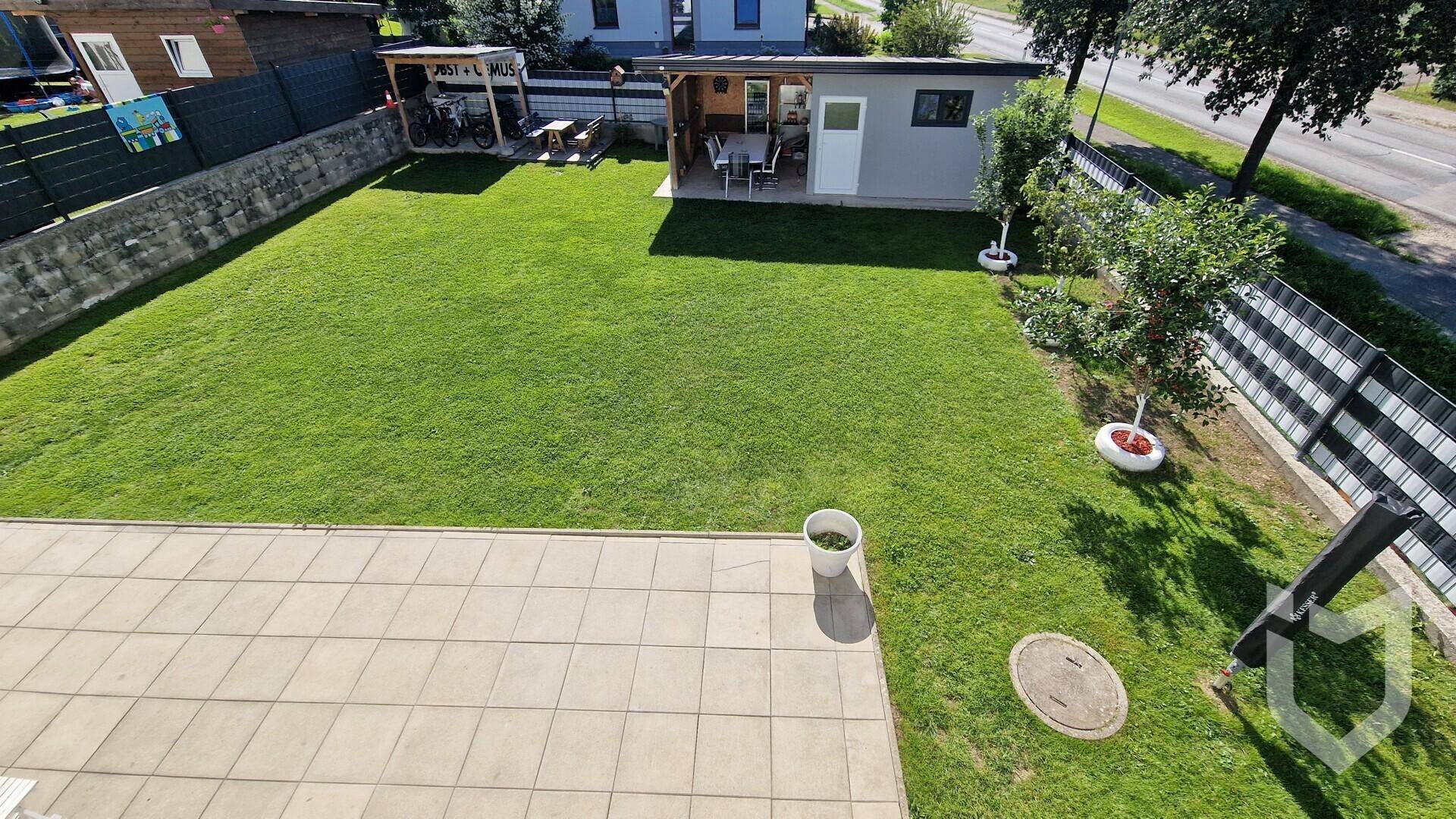 Vogelperspektive des Gartens mit großer Rasenfläche, Terrasse und Gartenhaus.