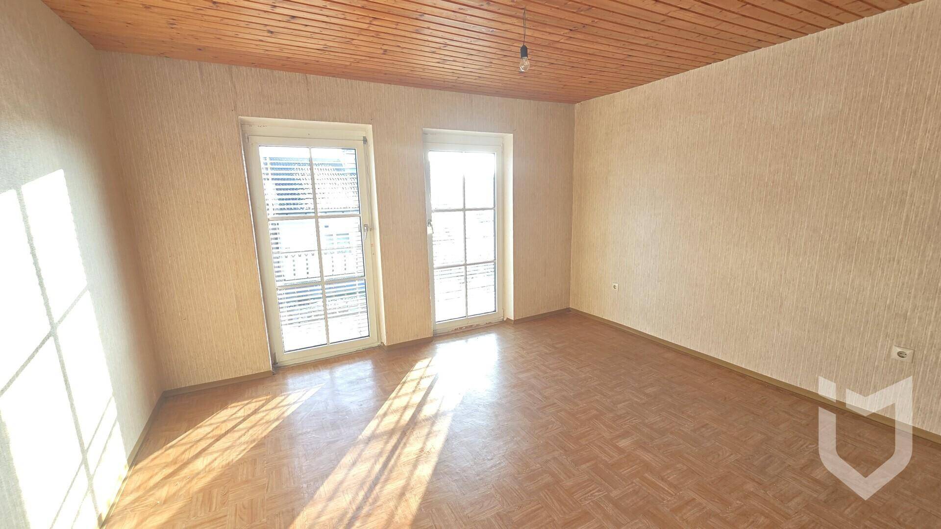 Helles Zimmer mit Parkettboden und zwei Fenstertüren, die Zugang zu einem Balkon bieten.