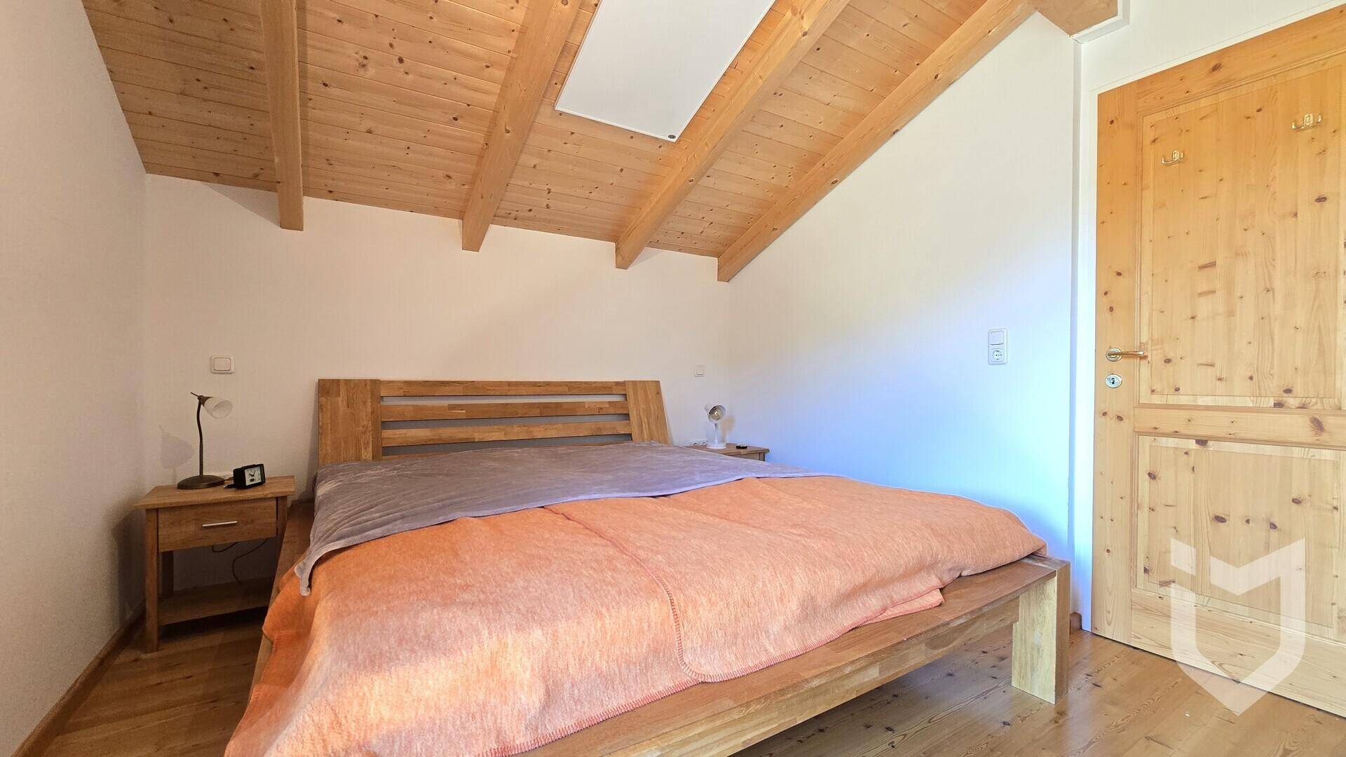 Schlafzimmer mit Holzbett, sichtbaren Dachbalken und einem Dachfenster für natürliches Licht.