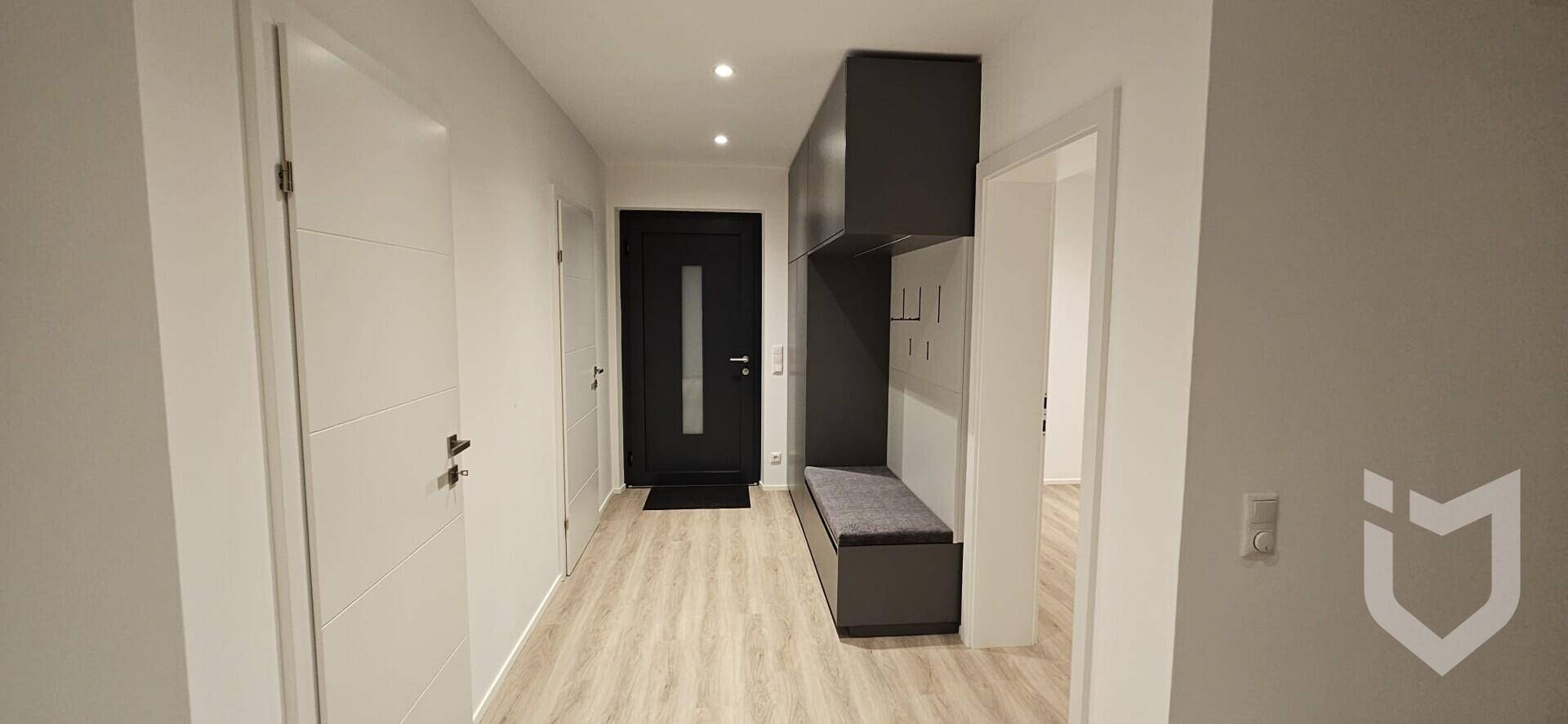 Heller Flur mit moderner Garderobe, dunkler Eingangstür und hellem Laminatboden.