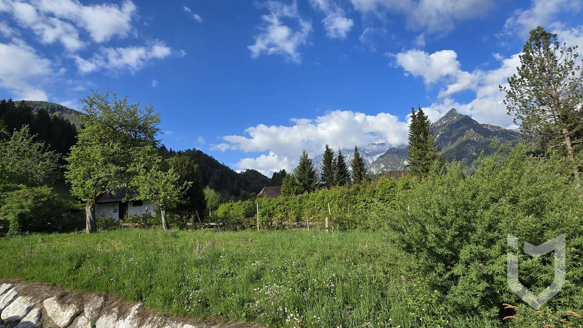 Weitläufiges, grünes Grundstück unter blauem Himmel mit beeindruckendem Panorama der Alpen.