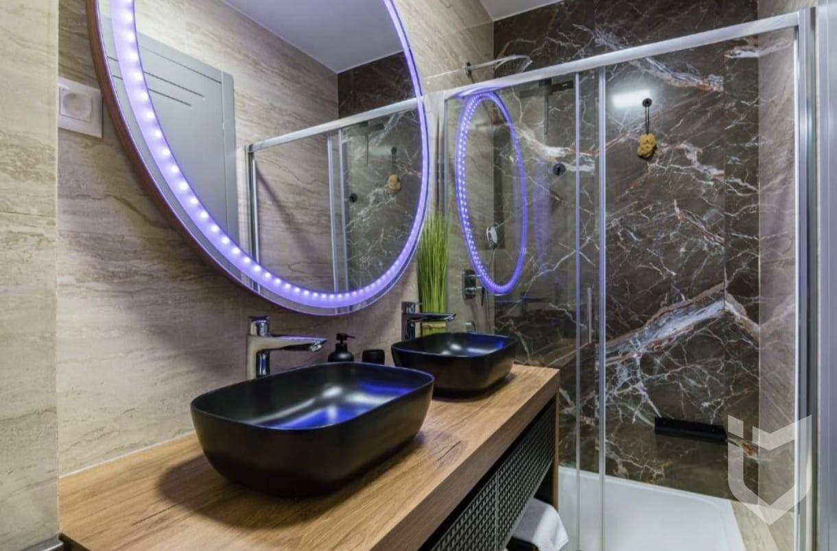 Modernes Badezimmer mit Doppelwaschbecken, beleuchtetem Spiegel und begehbarer Dusche.