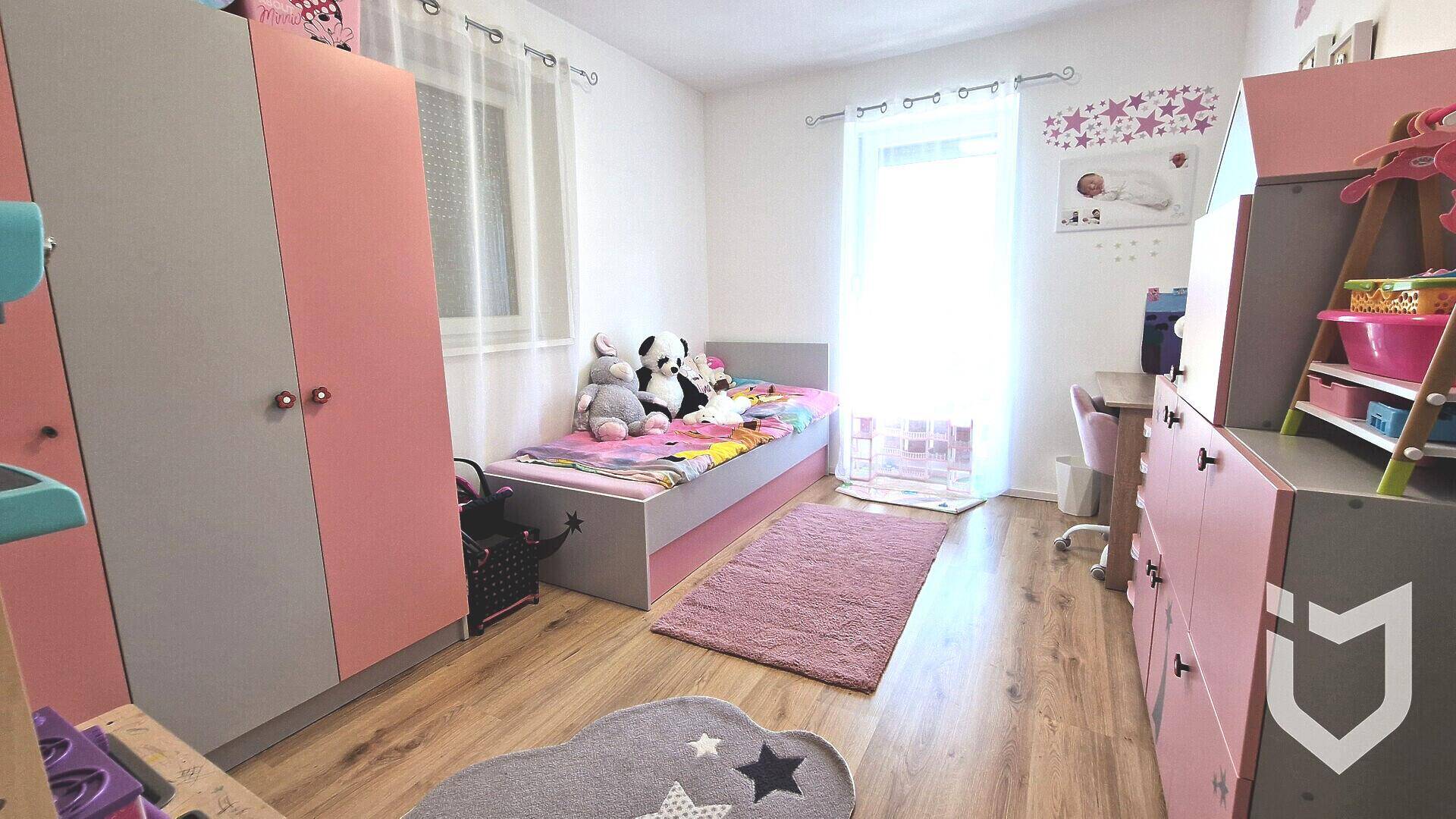 Freundliches Kinderzimmer in Rosa- und Grautönen mit Bett und Kleiderschrank.