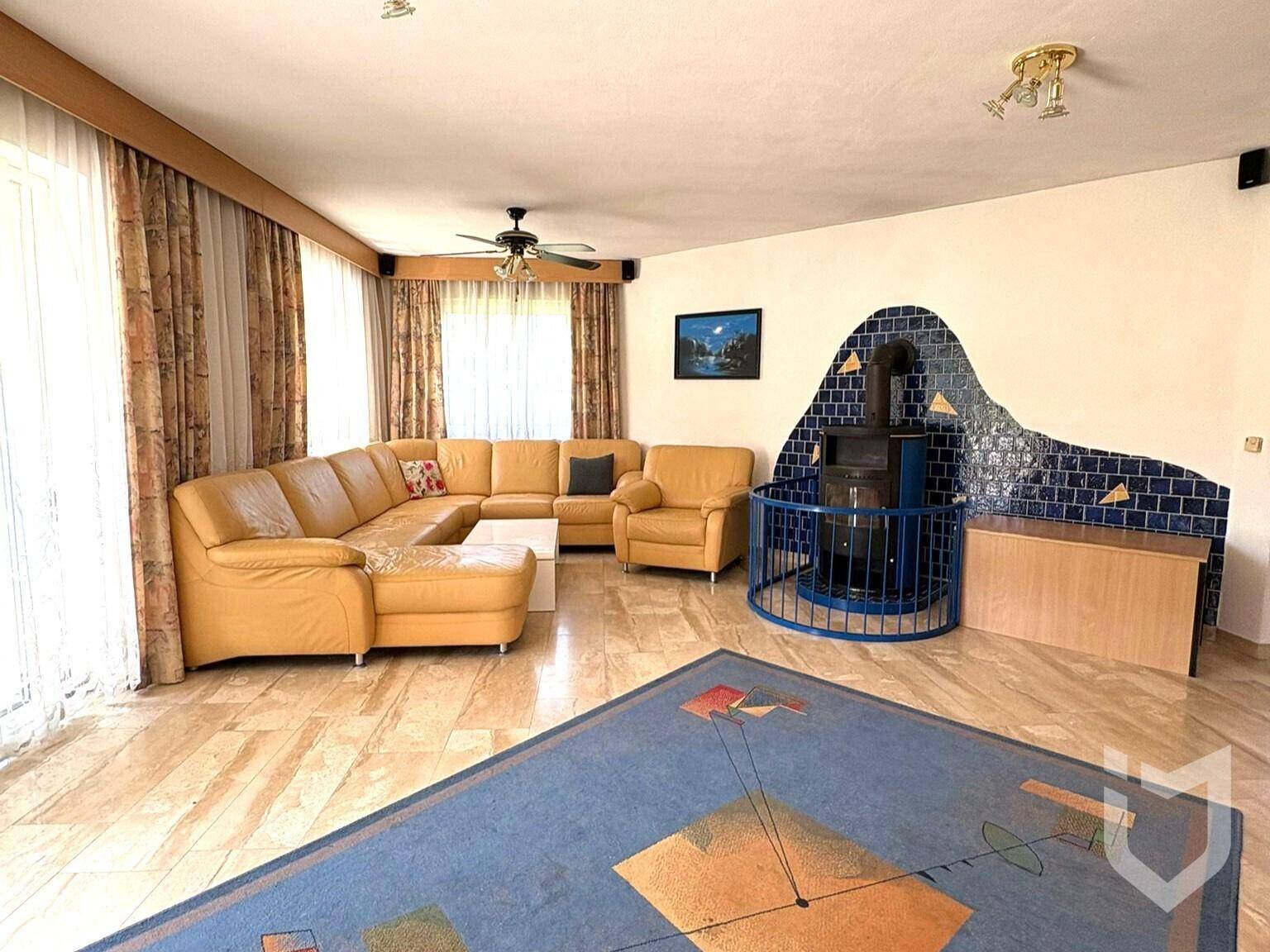 Geräumiges Wohnzimmer mit Ledersofa, Kaminofen und Fliesenboden.