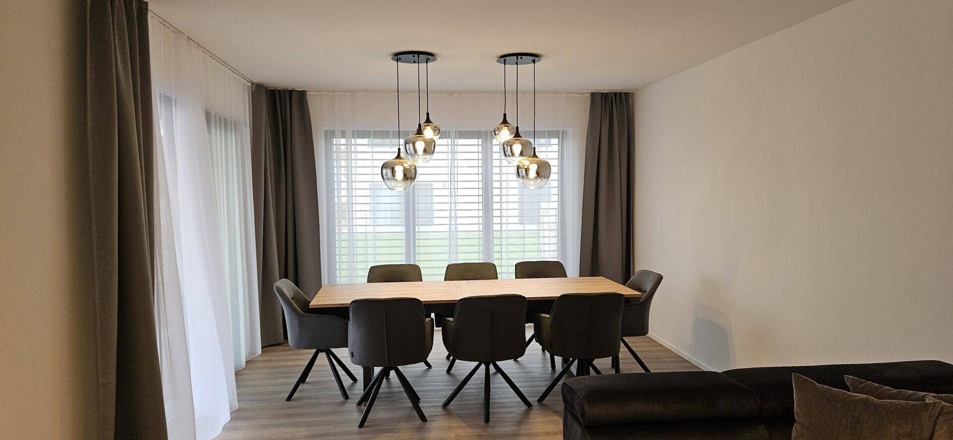 Heller Essbereich mit großem Holztisch, modernen Pendelleuchten und Blick ins Grüne.