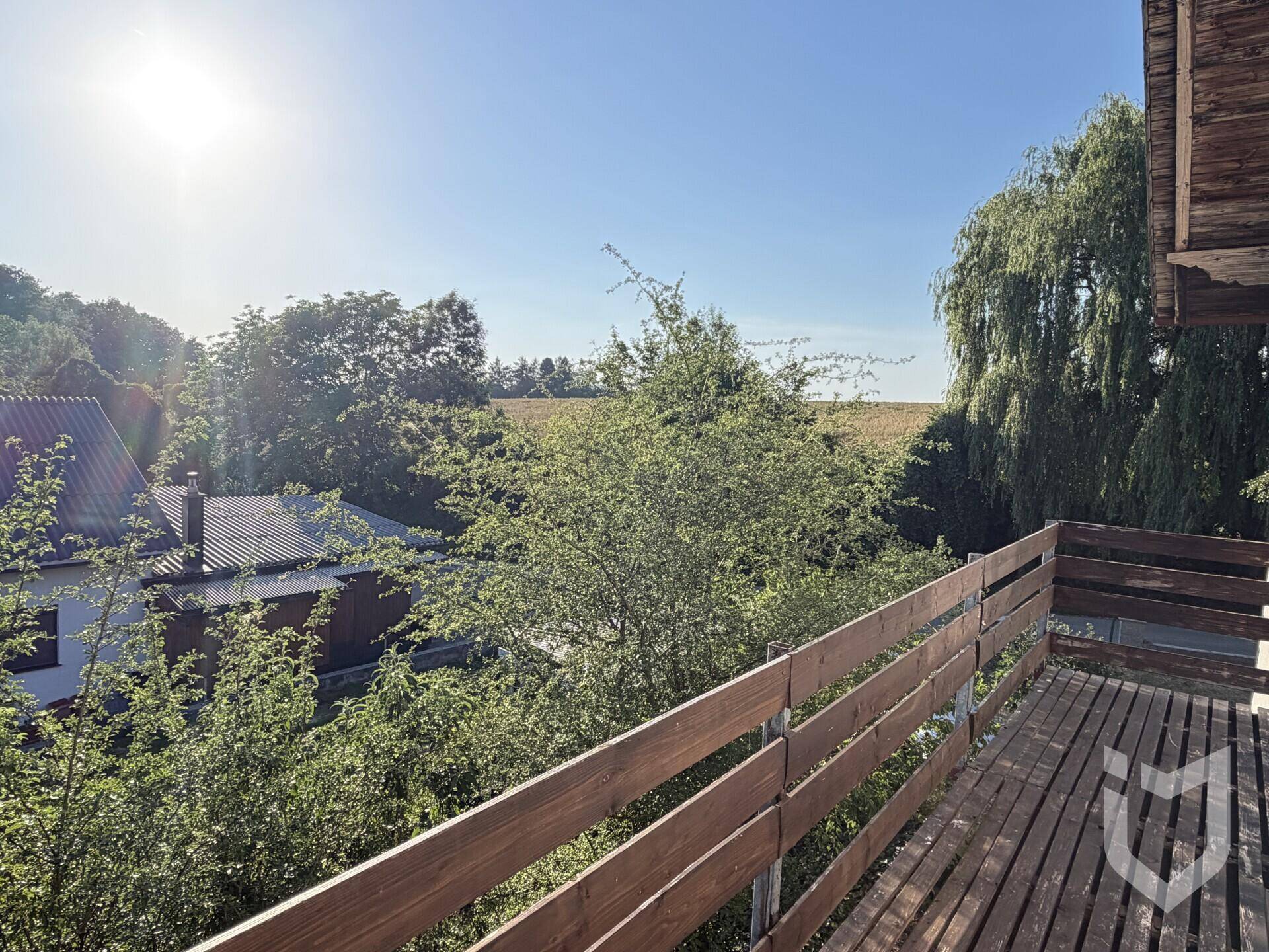 Sonniger Holzbalkon mit weitem Blick über Felder und Bäume in die Landschaft.