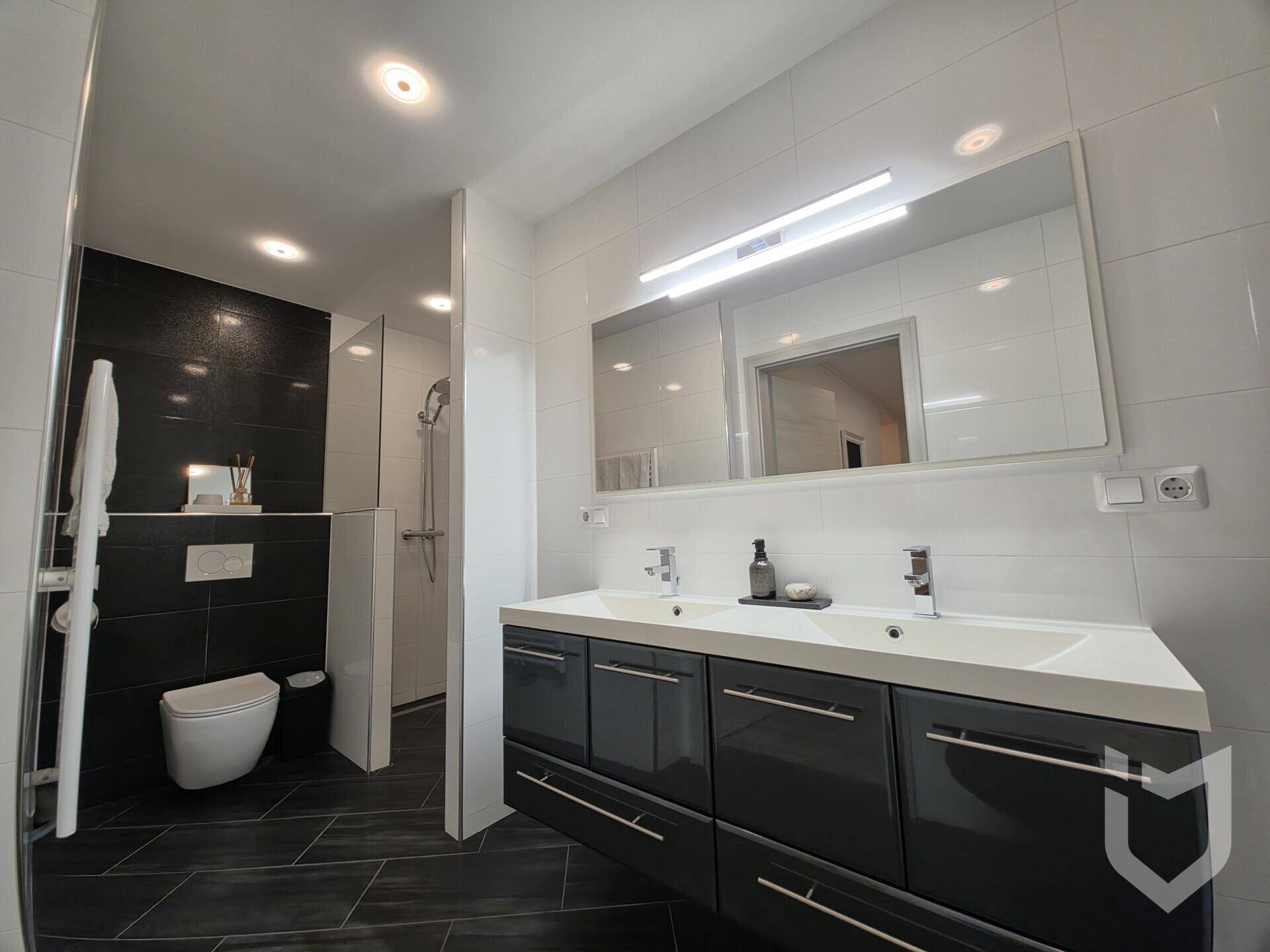 Modernes Badezimmer mit Doppelwaschbecken, großer Spiegelfläche und begehbarer Dusche.