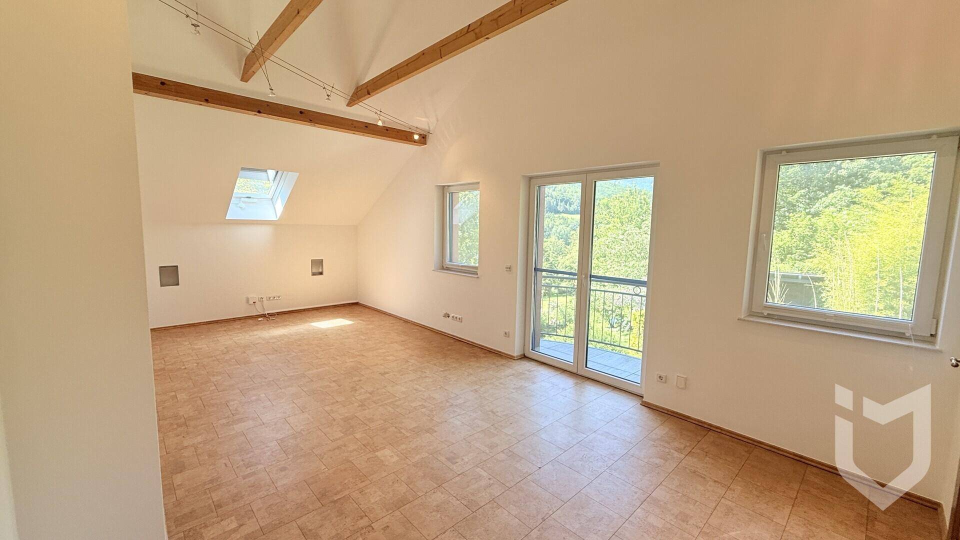 Heller Raum im Dachgeschoss mit sichtbaren Holzbalken, Dachfenster und französischem Balkon.