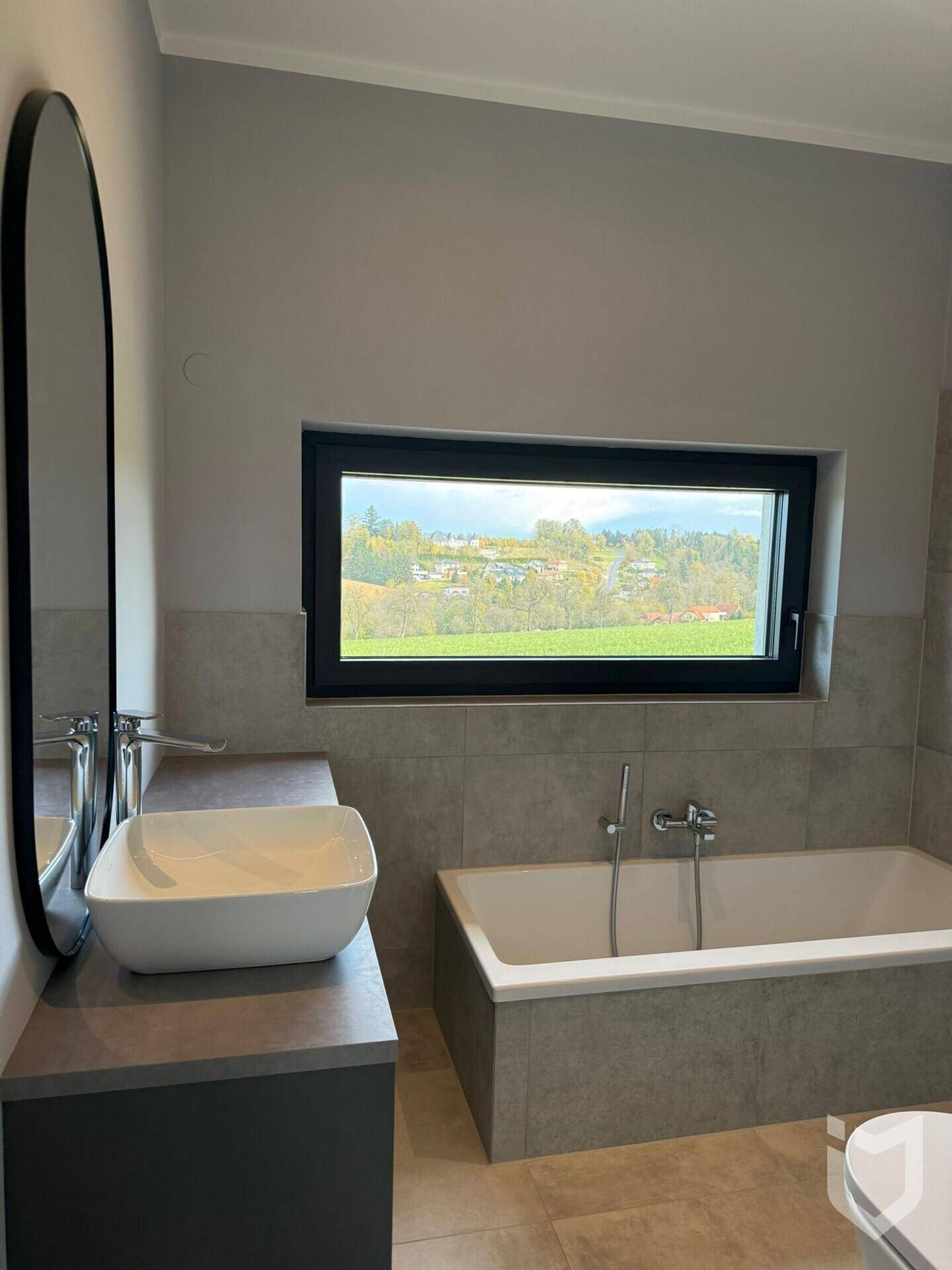 Modernes Badezimmer mit Badewanne, Einzelwaschbecken und Fenster mit Blick ins Grüne.