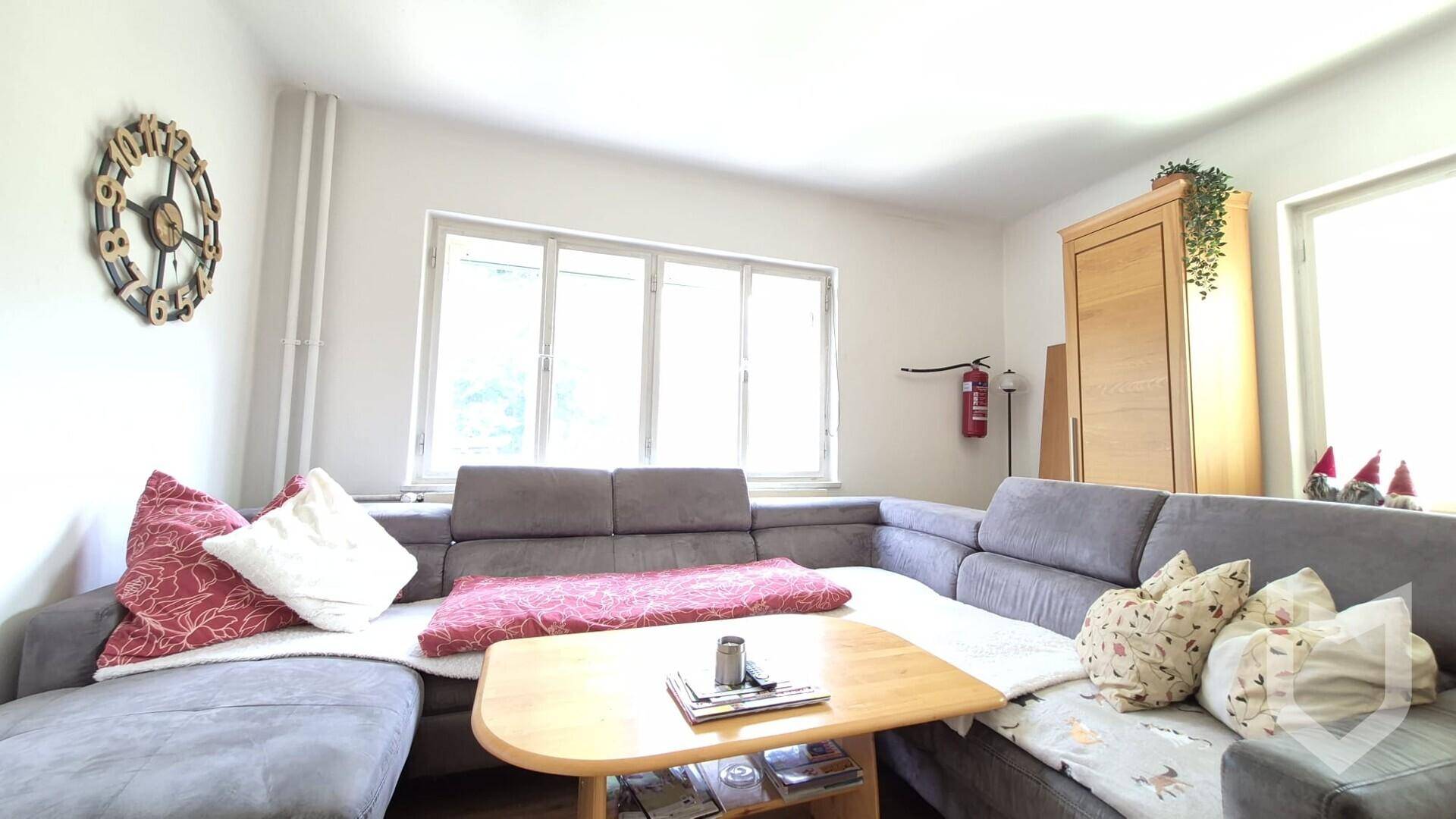 Gemütliches Wohnzimmer mit großem Ecksofa, Holztisch und viel Tageslicht durch das Fenster.