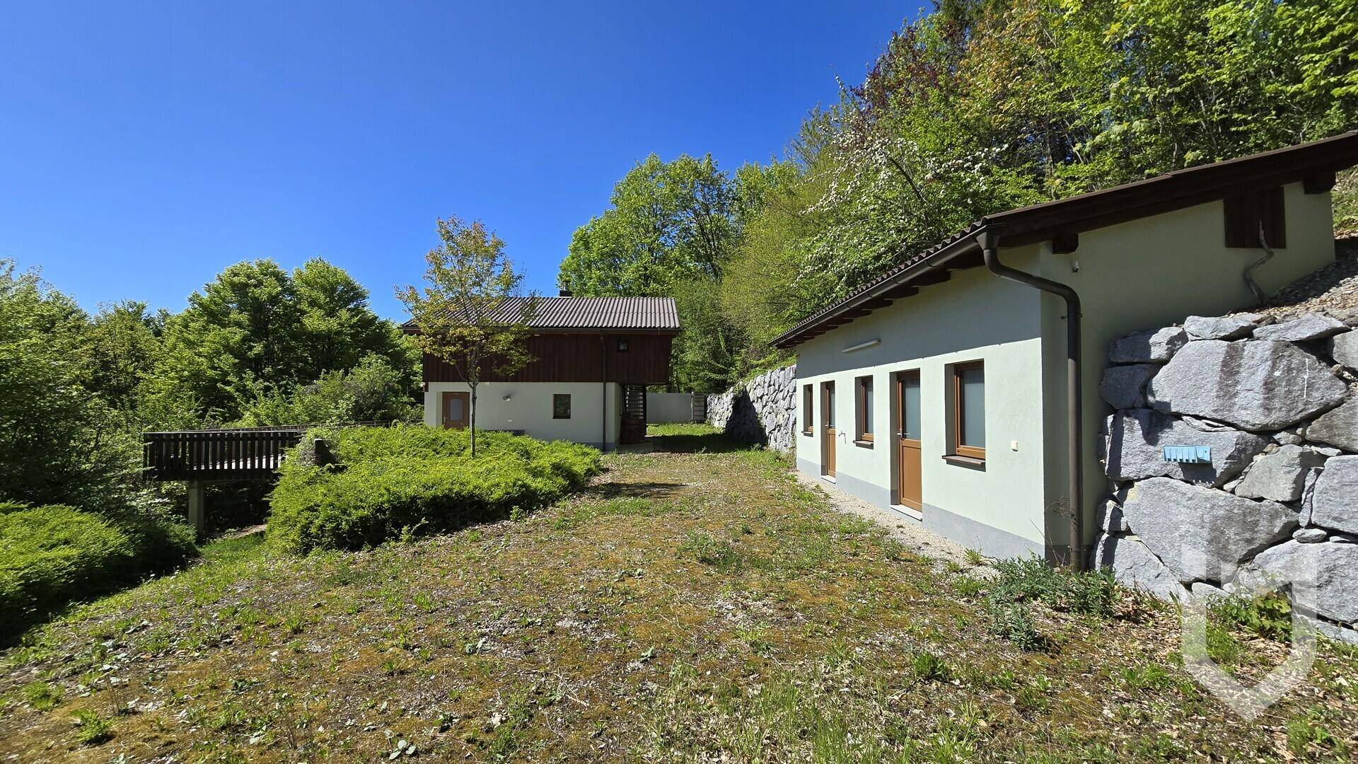 Gesamtansicht des Anwesens mit Haupthaus und Nebengebäude, umgeben von viel Grünfläche und Bäumen.