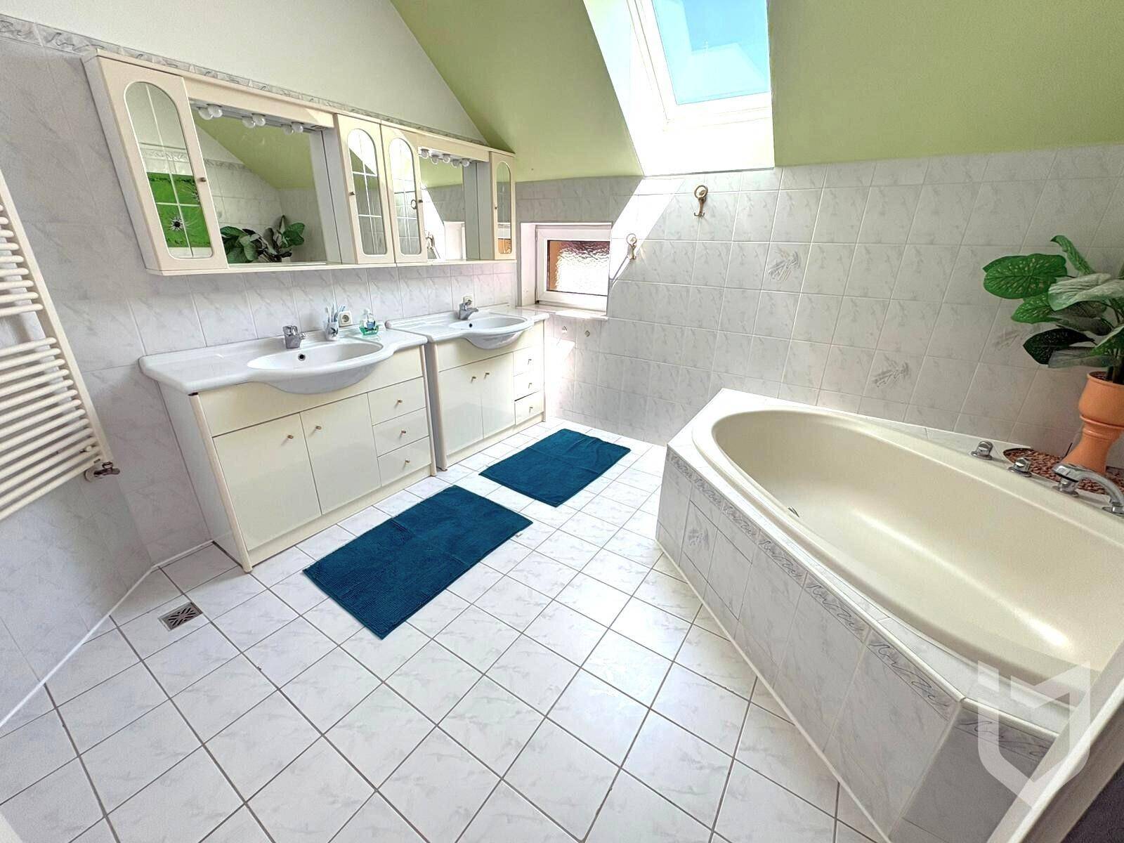 Helles Badezimmer mit Doppelwaschbecken, Badewanne und Dachfenster.