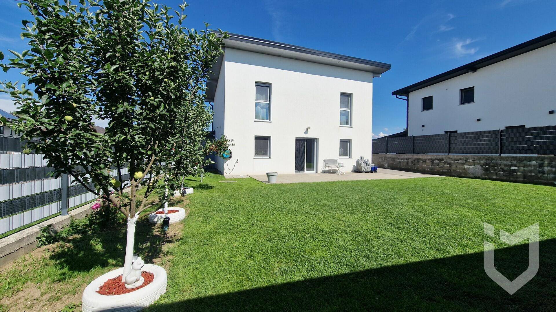 Weitläufiger, gepflegter Garten mit Rasenfläche und jungen Obstbäumen hinter dem Haus.