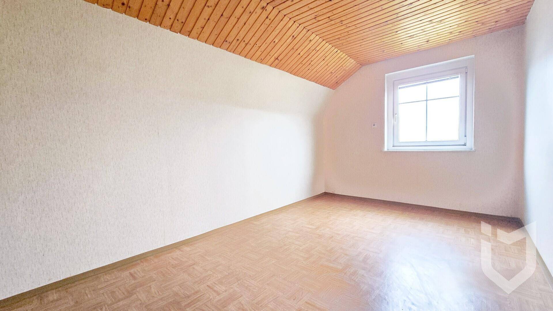 Dachzimmer mit schräger Holzdecke und einem Fenster, das den Raum mit natürlichem Licht versorgt.