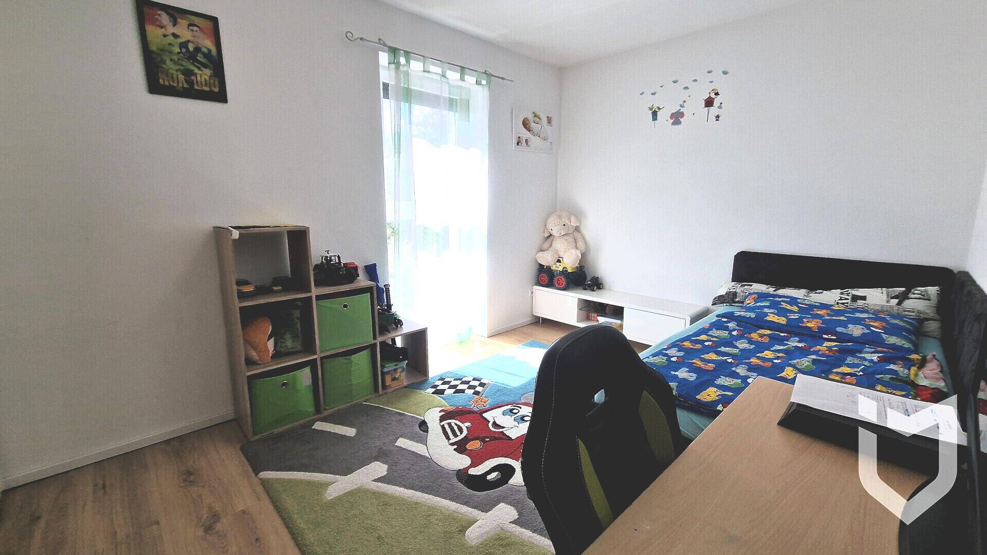 Helles Kinderzimmer mit Holzboden, Schreibtisch und Spielteppich.