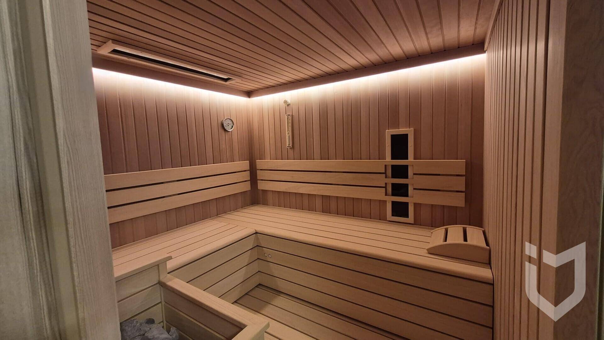 Innenansicht der Holzsauna mit bequemen Bänken und indirekter Beleuchtung für Entspannung.