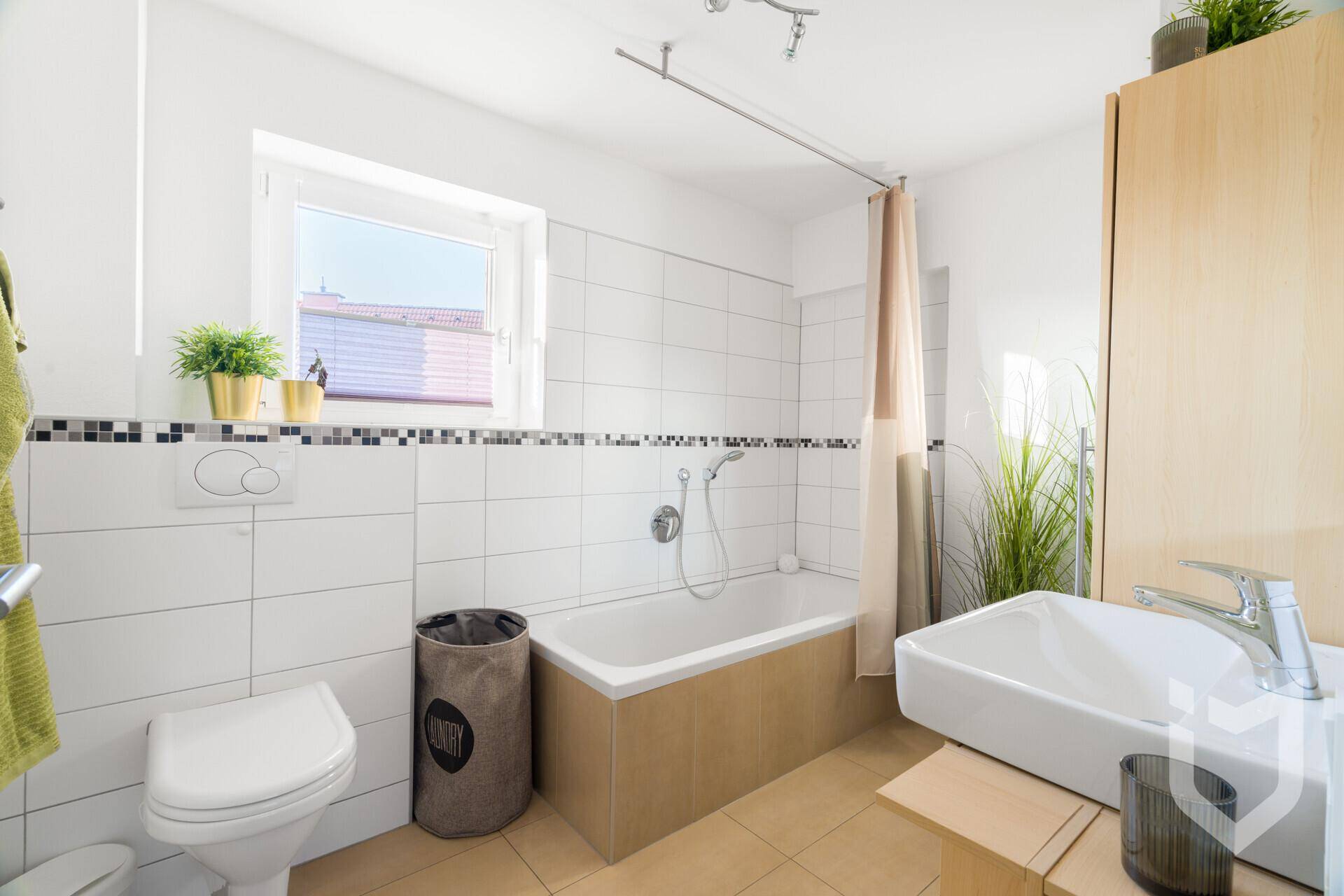 Helles Badezimmer mit Badewanne, WC, Einzelwaschbecken und Fenster.