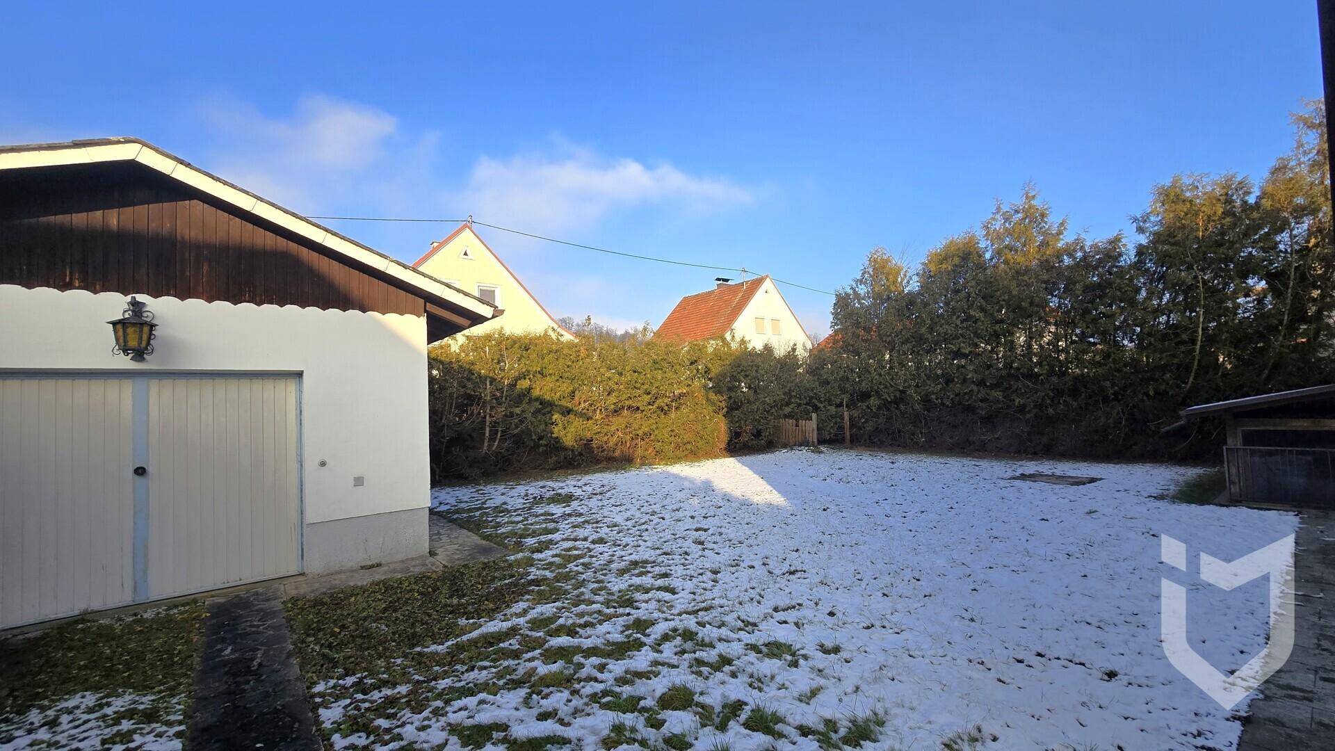 Großer Gartenbereich hinter dem Haus mit Rasenfläche, Hecken und einer Garage im Hintergrund.