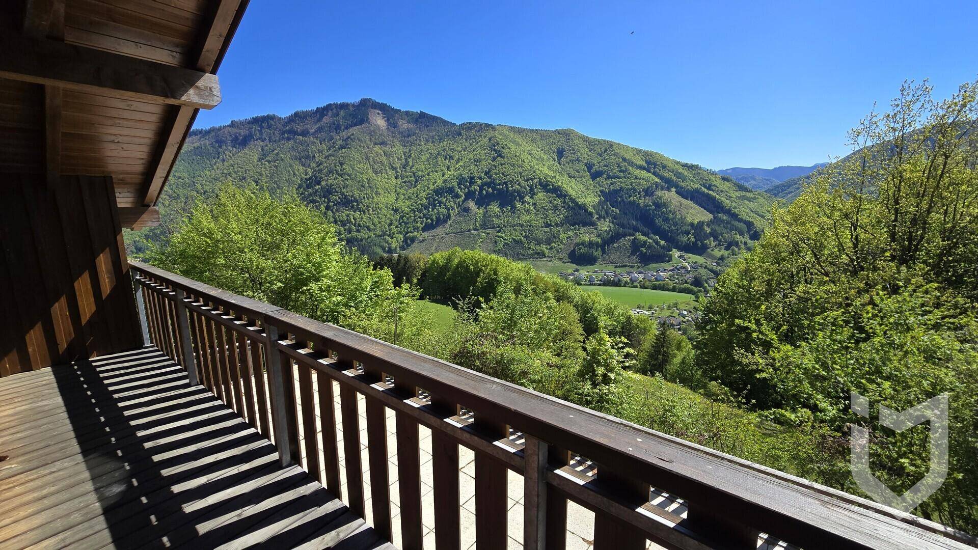 Holzbalkon mit rustikalem Geländer und weitem Blick auf die bewaldeten Berge und das Tal.