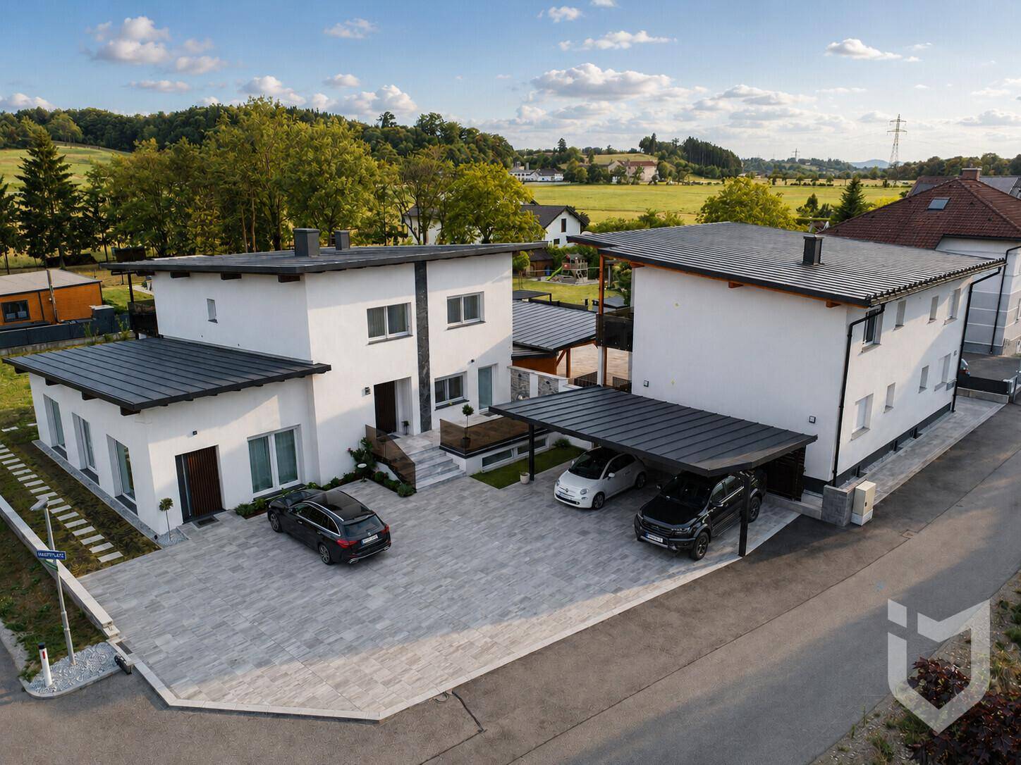 Vogelperspektive auf zwei moderne Wohnhäuser mit Carports und großzügiger gepflasterter Zufahrt.