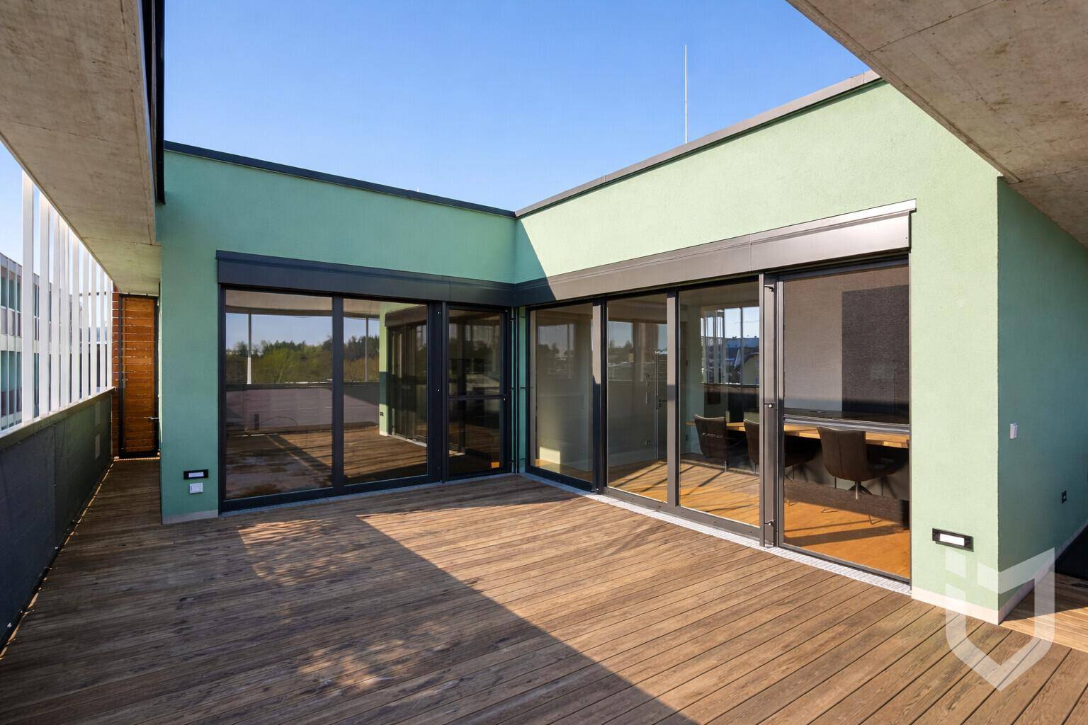 Geräumige Dachterrasse mit Holzdeck und großen Glasfronten, die viel Platz im Freien bietet.