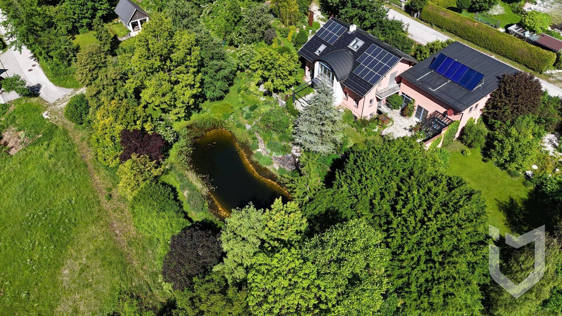 Weitläufige Luftaufnahme eines Landhauses mit Solaranlagen, eingebettet in eine grüne Landschaft mit Teich.