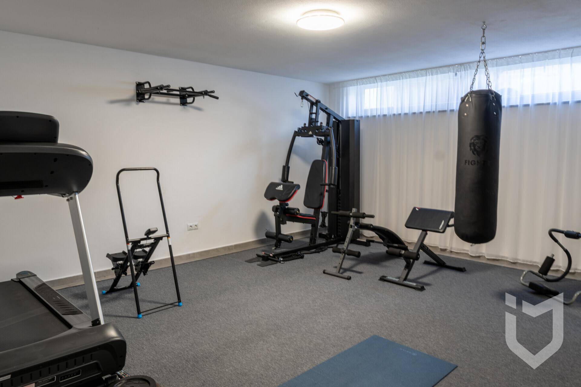 Geräumiger Fitnessraum mit verschiedenen Trainingsgeräten und Fenster für Belüftung.