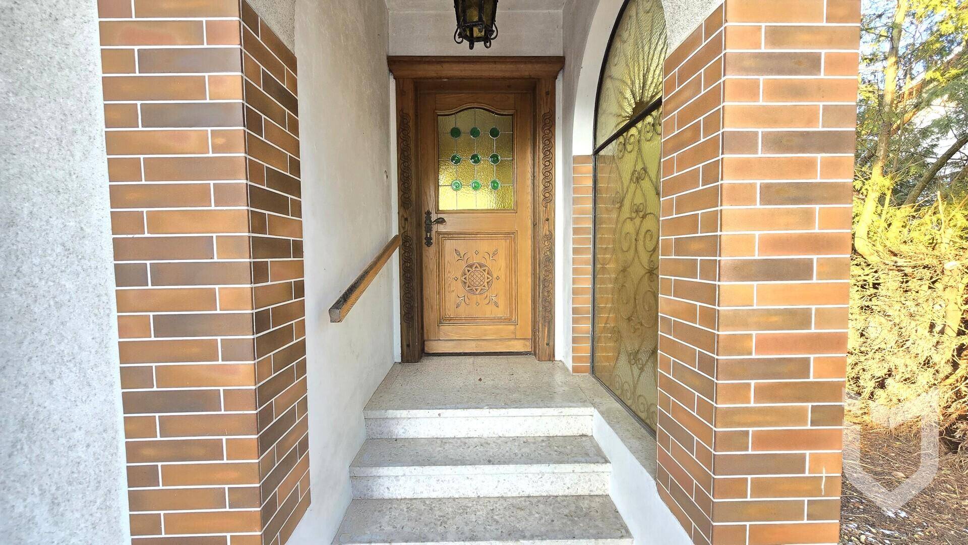 Traditioneller Eingangsbereich mit einer Holztür, dekorativen Glasfenstern und Ziegelverkleidung.