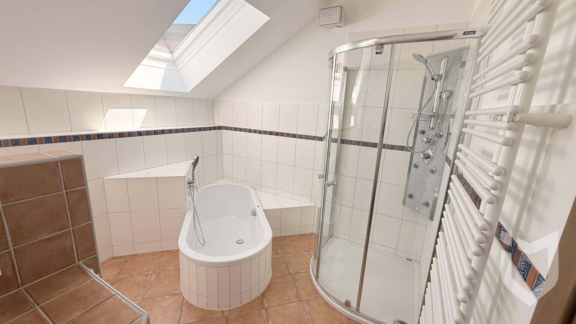Badezimmer mit kleiner Badewanne, Eckdusche, beheiztem Handtuchhalter und Dachfenster.