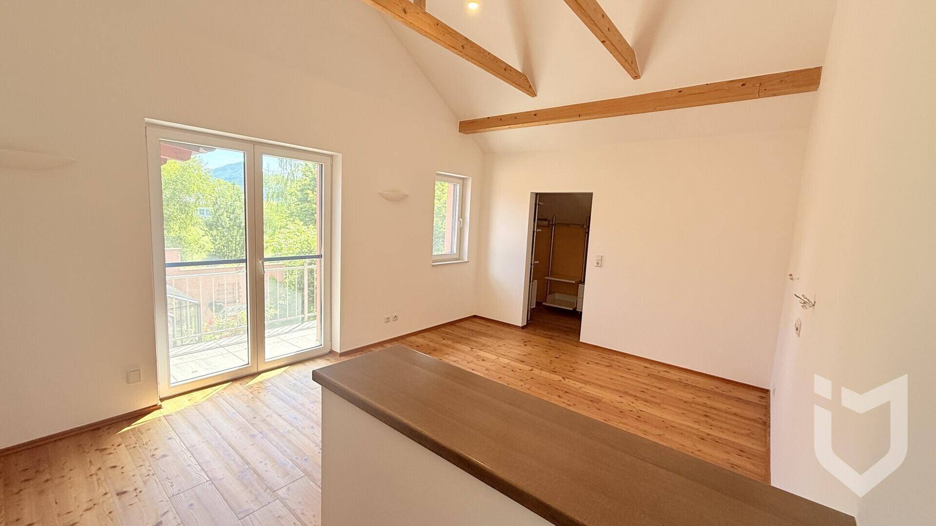 Schlafzimmer mit Holzdielenboden, sichtbaren Holzbalken und Zugang zu einem begehbaren Kleiderschrank.