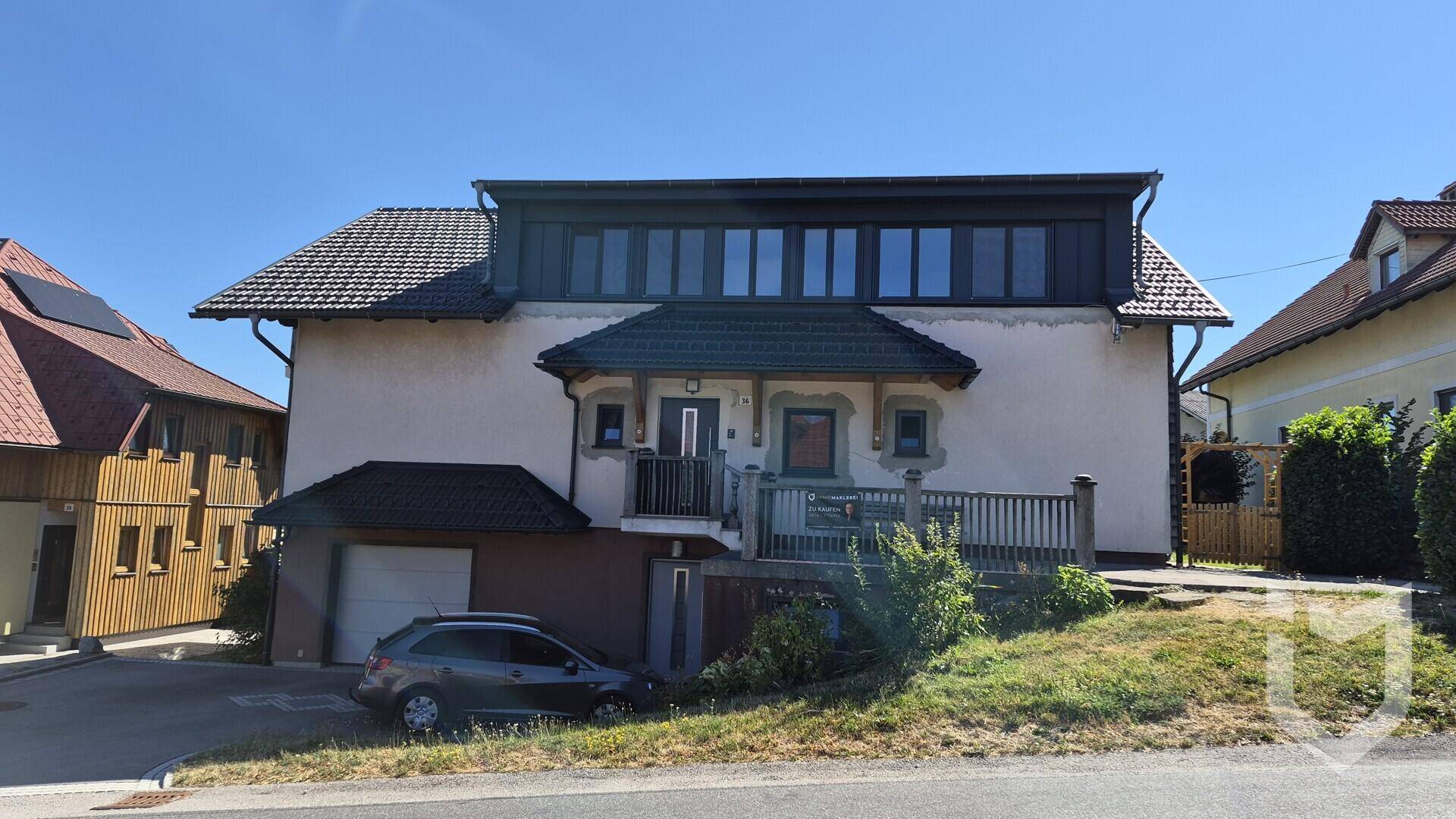 Vorderansicht des Hauses mit traditioneller Architektur, Balkon und Garage, umgeben von grüner Landschaft.