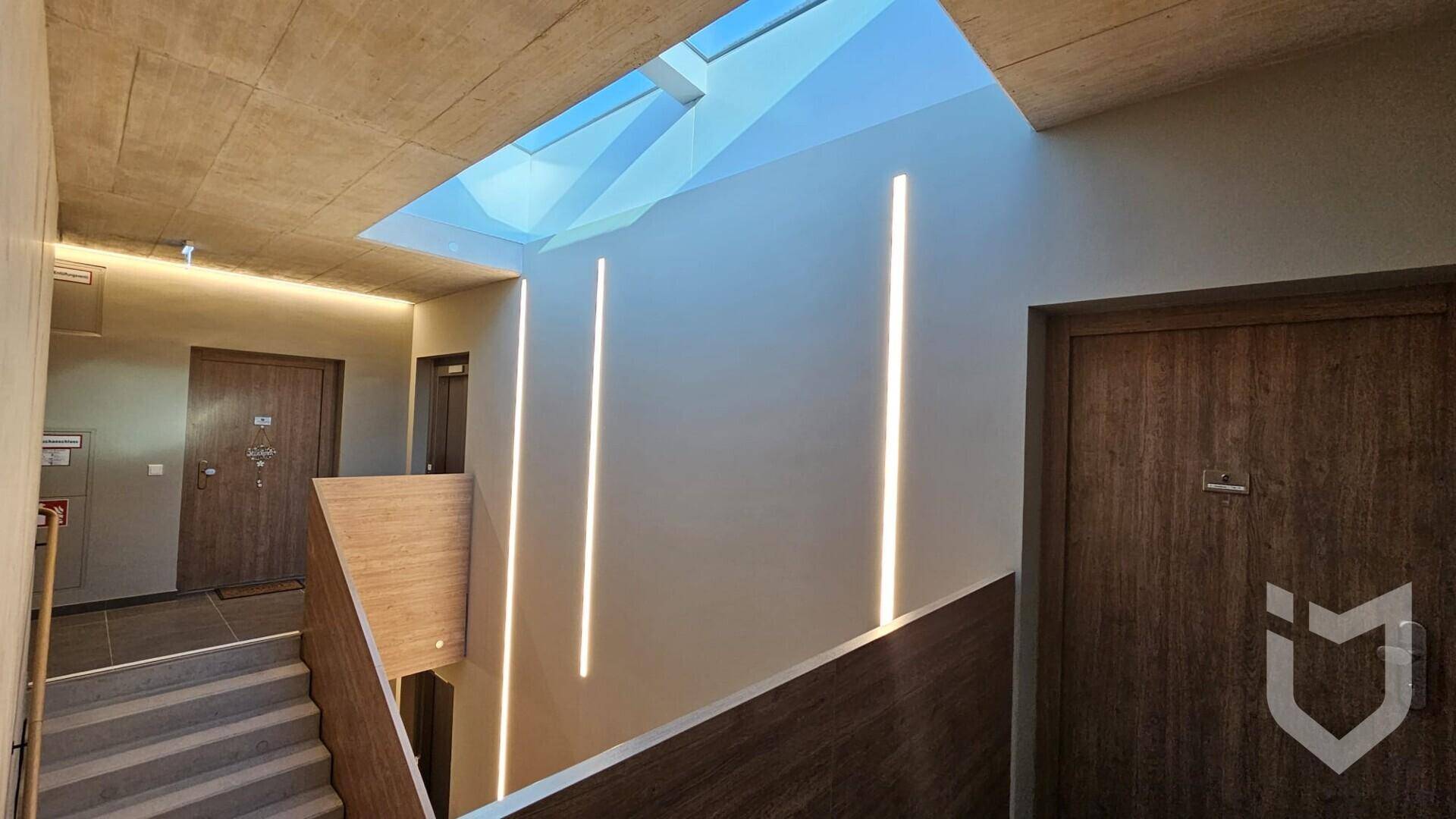 Modernes Treppenhaus mit eleganten Lichtleisten, Holzgeländer und einem hellen Oberlicht.