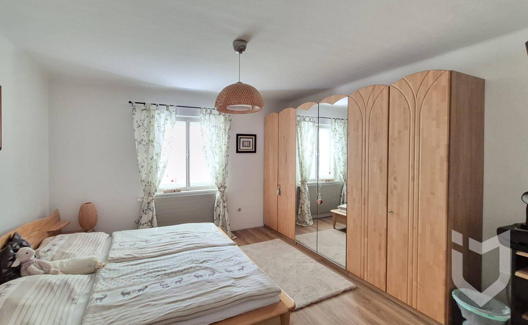 Schlafzimmer mit Doppelbett, großem Spiegelschrank und Fenstern mit Vorhängen.